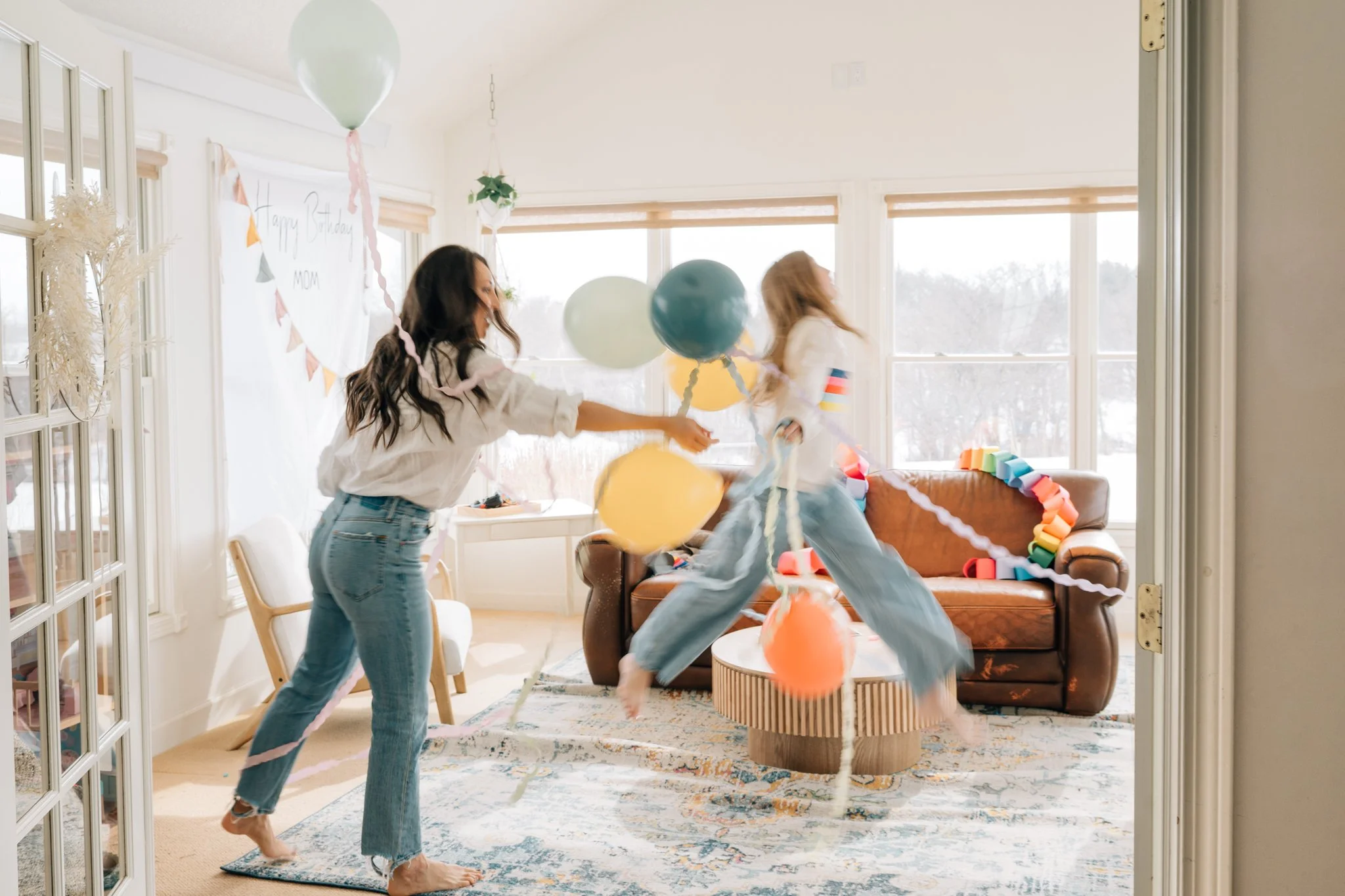 Intentionally blurry photo of a girl jumping holding lots of balloons as she celebrates her mom's birthday in their home during a lifestyle photography session.