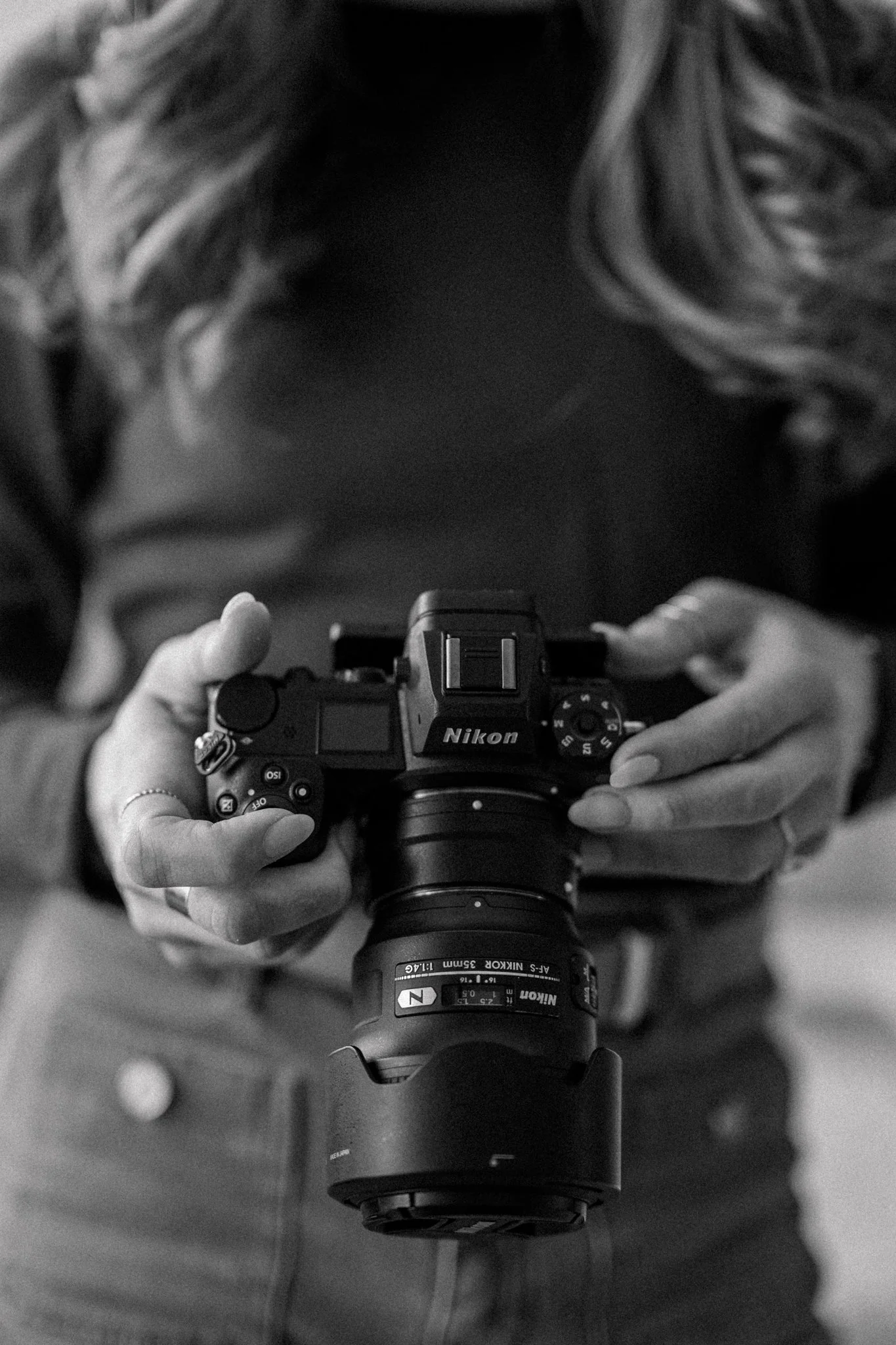 Detail photo of Claire holding her Nikon camera in black and white.