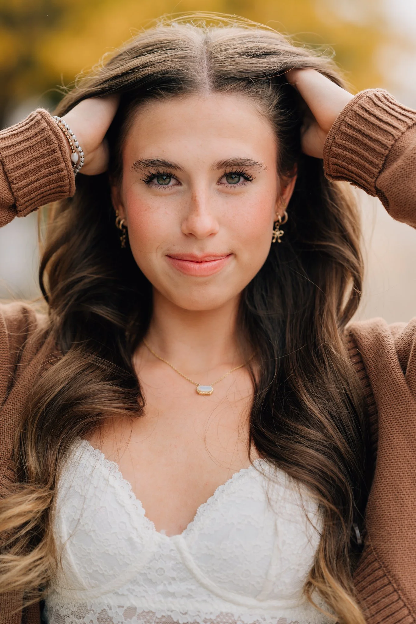 Close up of a girl in brown sweater, posing for her senior pictures in Omaha with changing leaves behind her. 