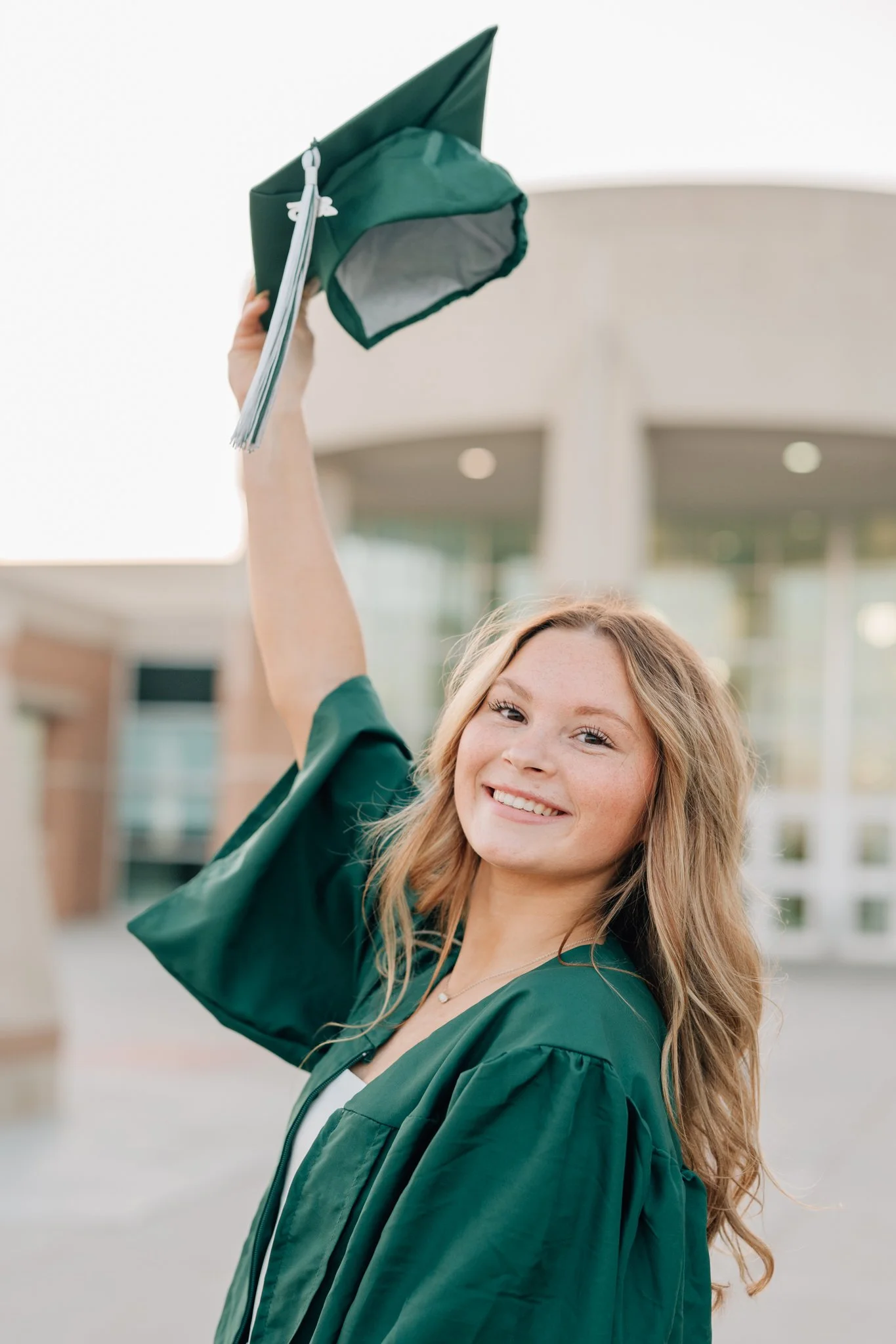 Girl lifts her green cap up in celebration of her graduation during cap and gown photoshoot.