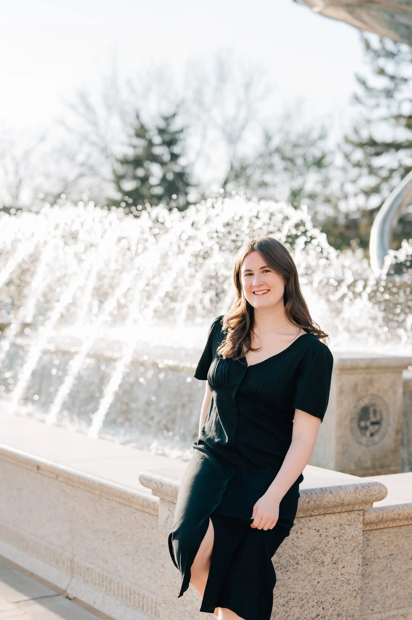 Image of Creighton graduate sitting on corner of fountain in front of St. John's during her college graduation pictures.