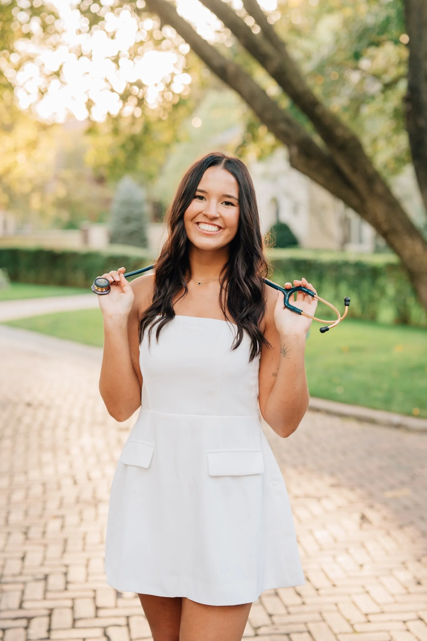 Nursing student poses with her stethoscope in a white dress to celebrate graduation.