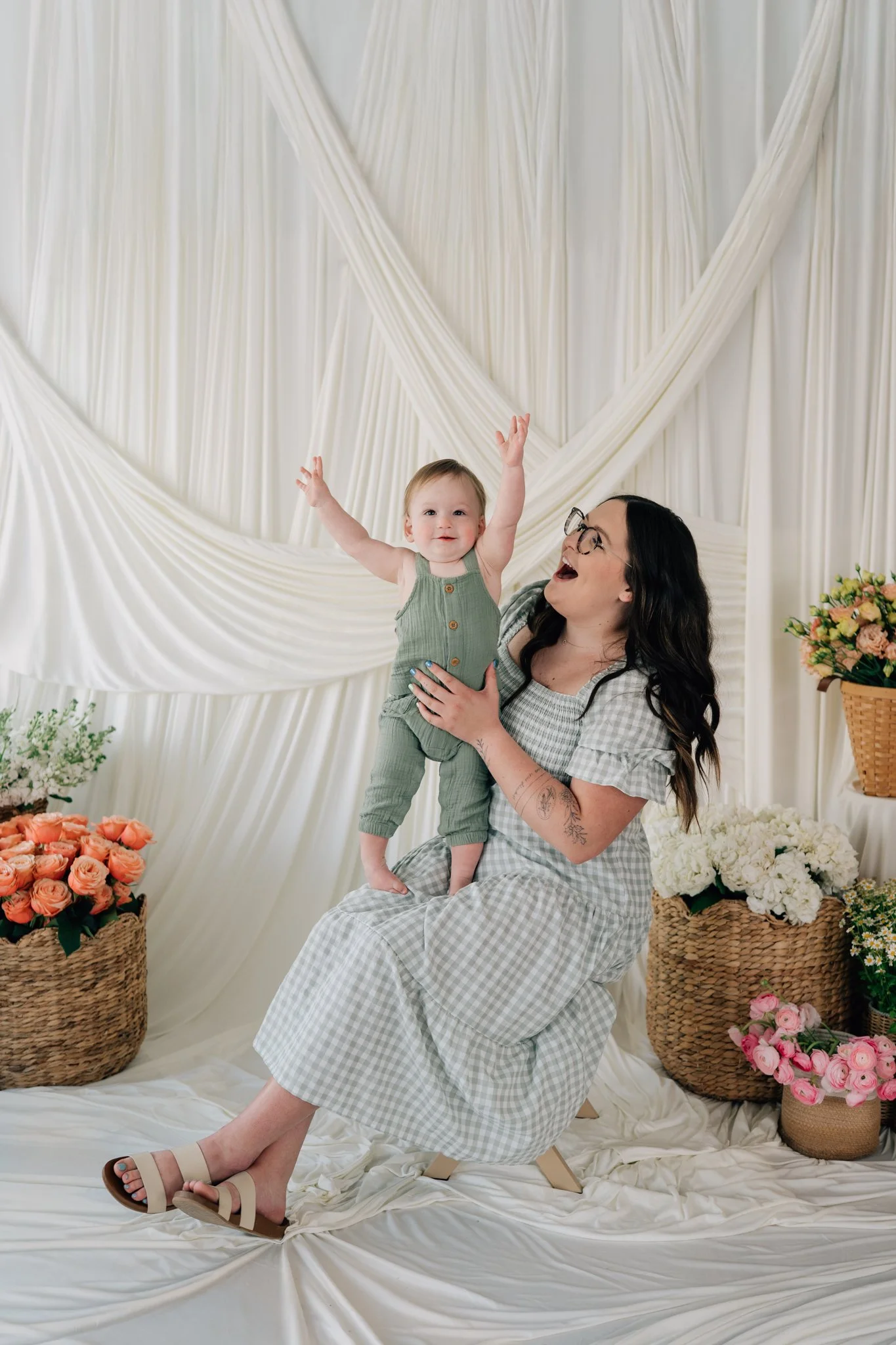 Little boy plays with mom during motherhood session among beautiful flowers in a studio.