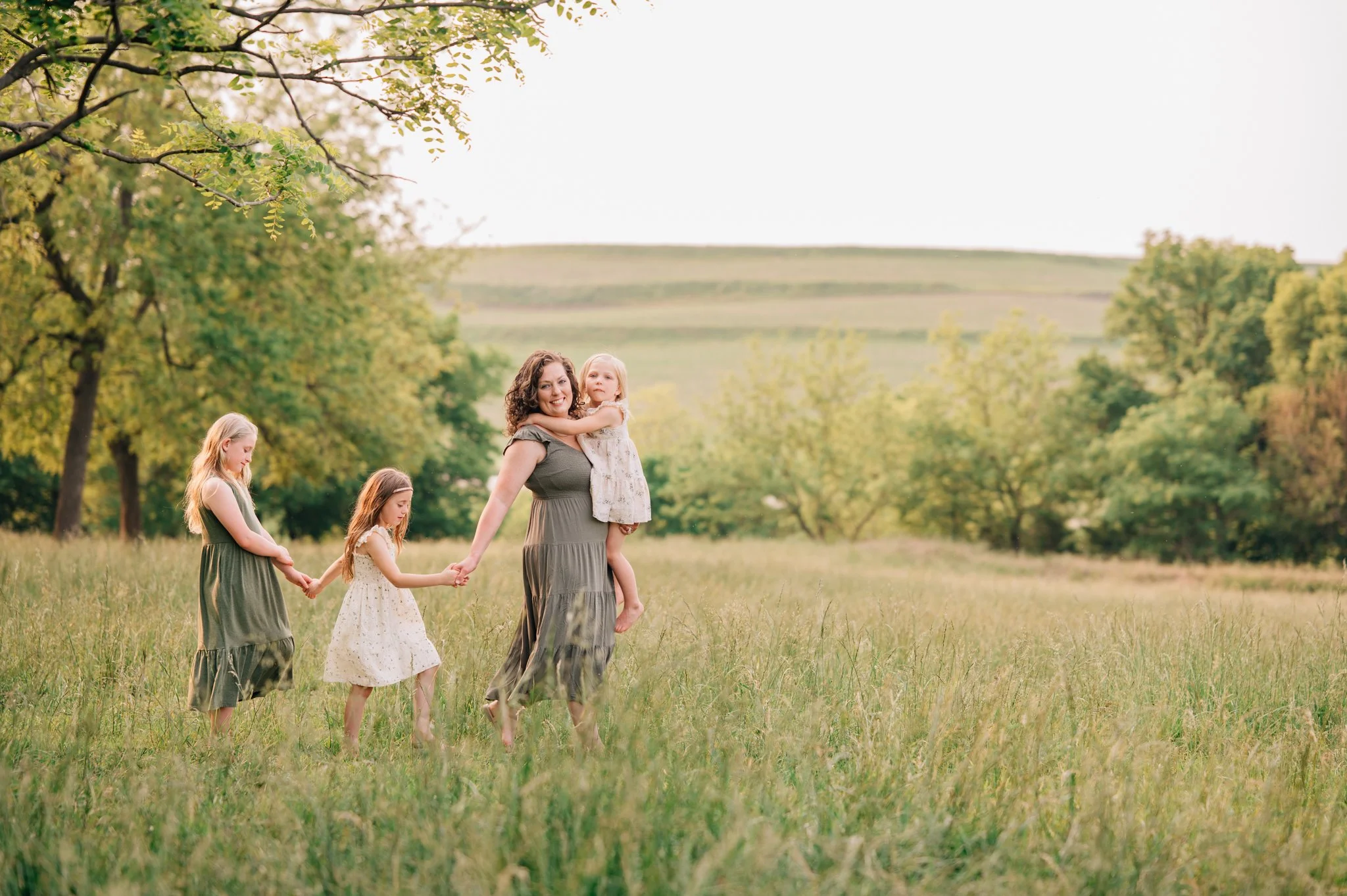 Mother leads her daughters though a pasture during family photos in Iowa.