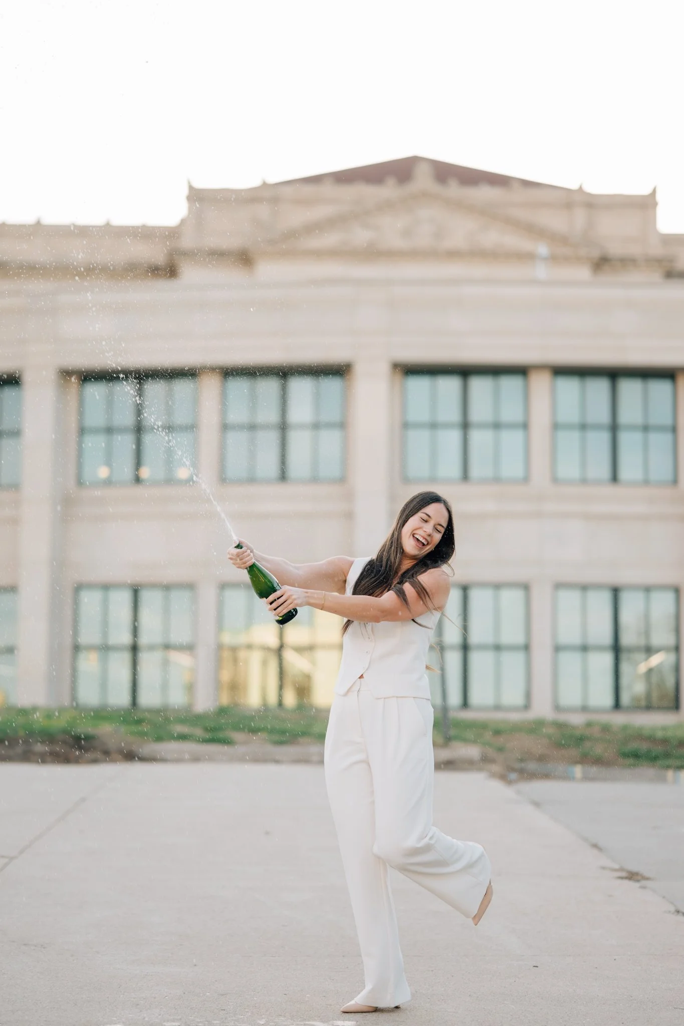 College graduate pops champagne during college graduation photo session in Omaha.
