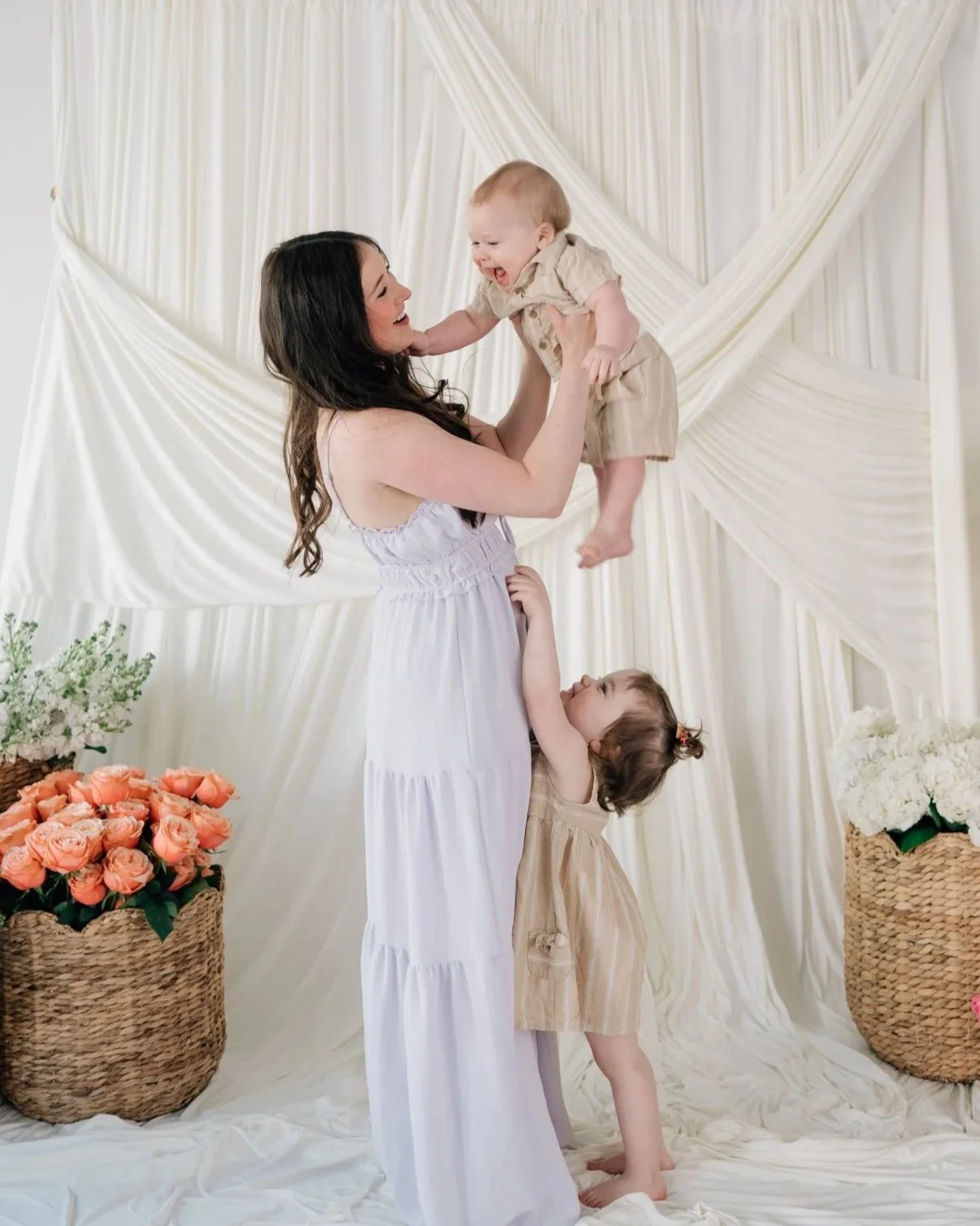 Big sister tries to tickle her little brother as mom plays with her little ones during a motherhood photo session for Mother's Day.