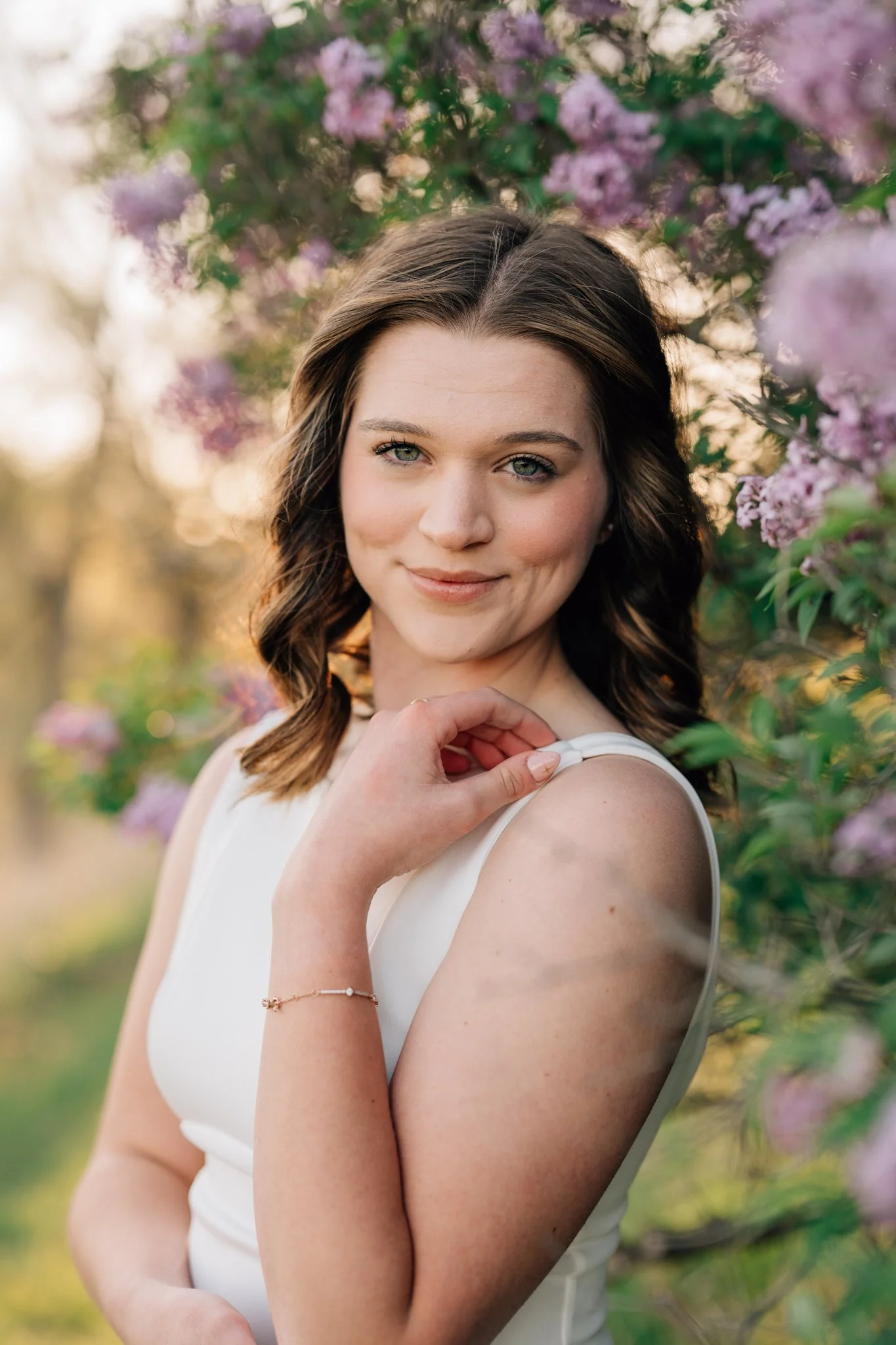 Girl in white dress poses near lilacs for graduation photos on college campus.