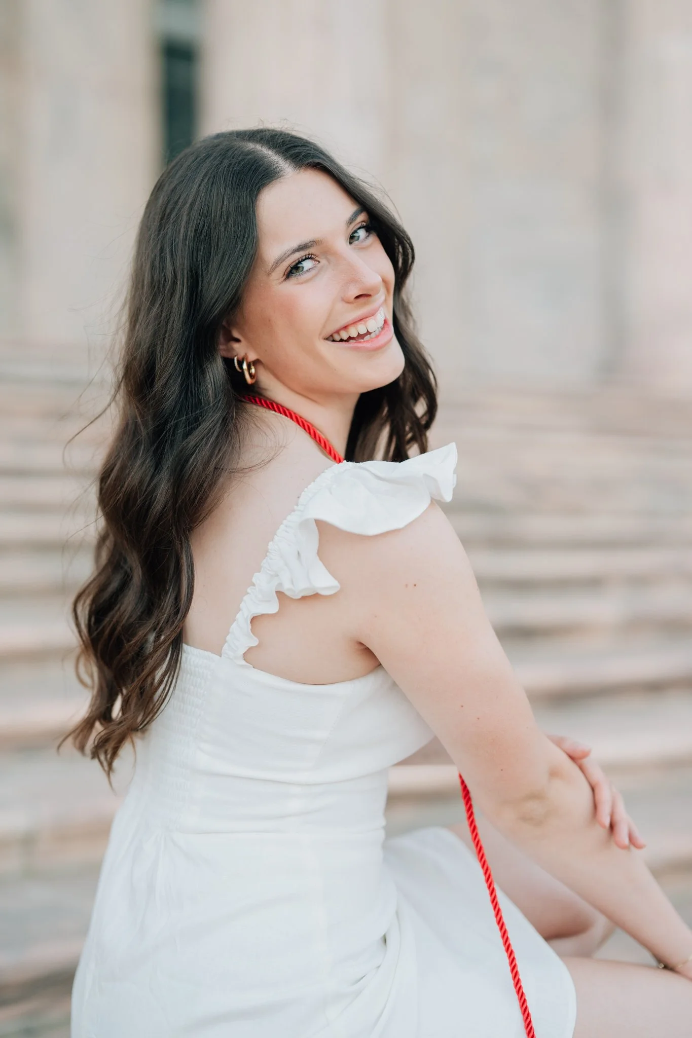 Girl poses in her honor cord and a white dress for her cap and gown graduation photos.