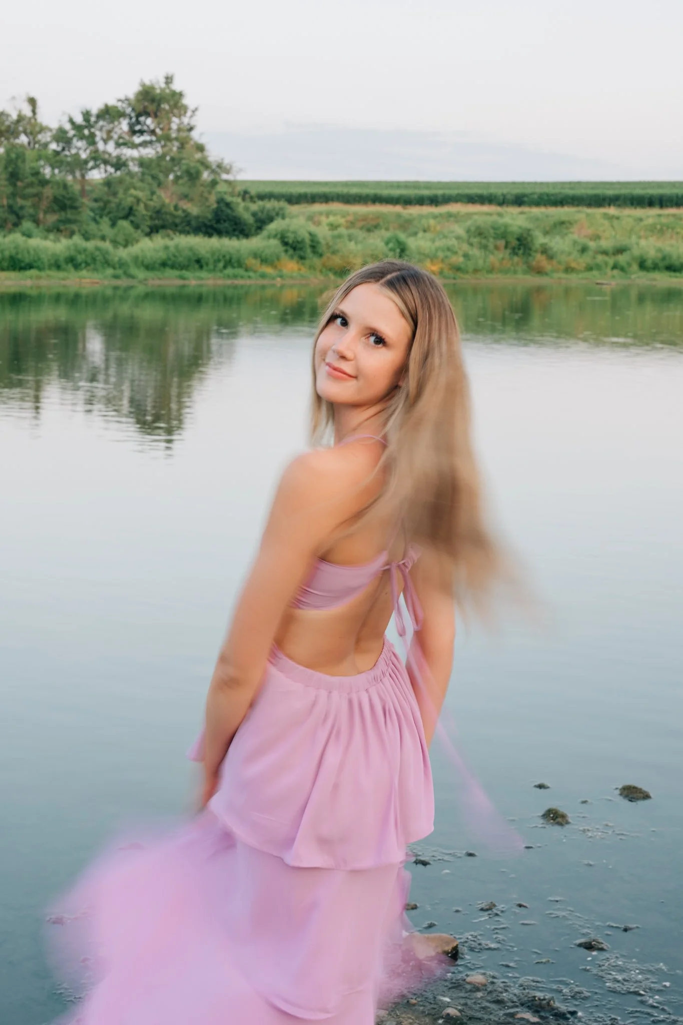 Motion blur image of a girl in a purple dress twirling in front of a lake for her senior pictures.