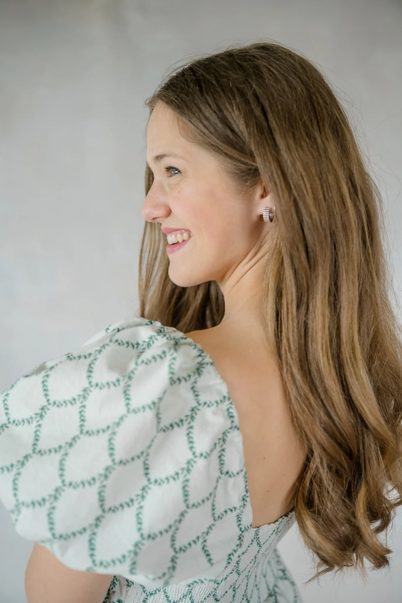 Professional headshot of woman looking off camera, wearing white and green dress.