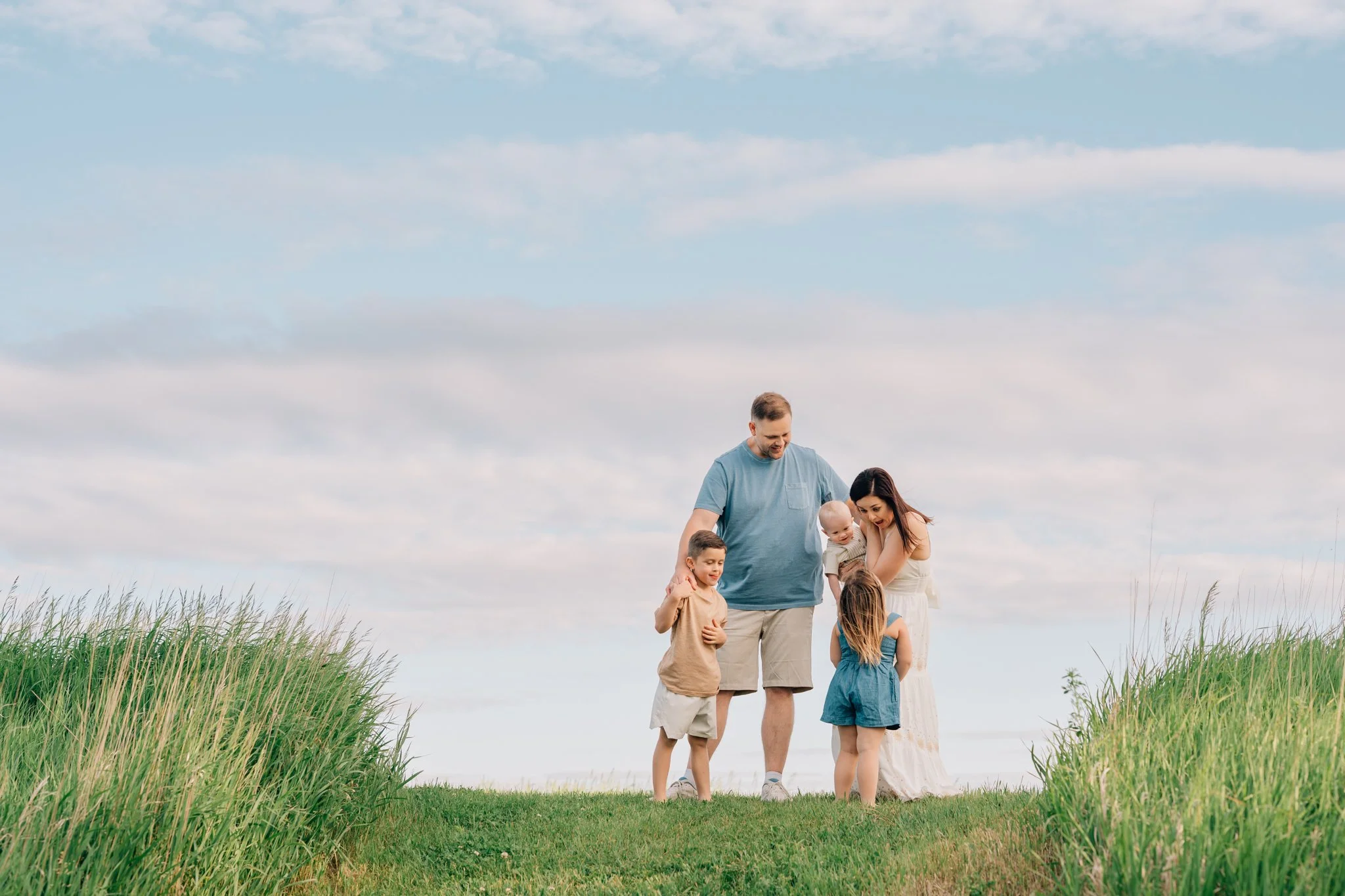 Family cuddles up at the top of a hill with a beautiful summer sky behind them during family photo session. 
