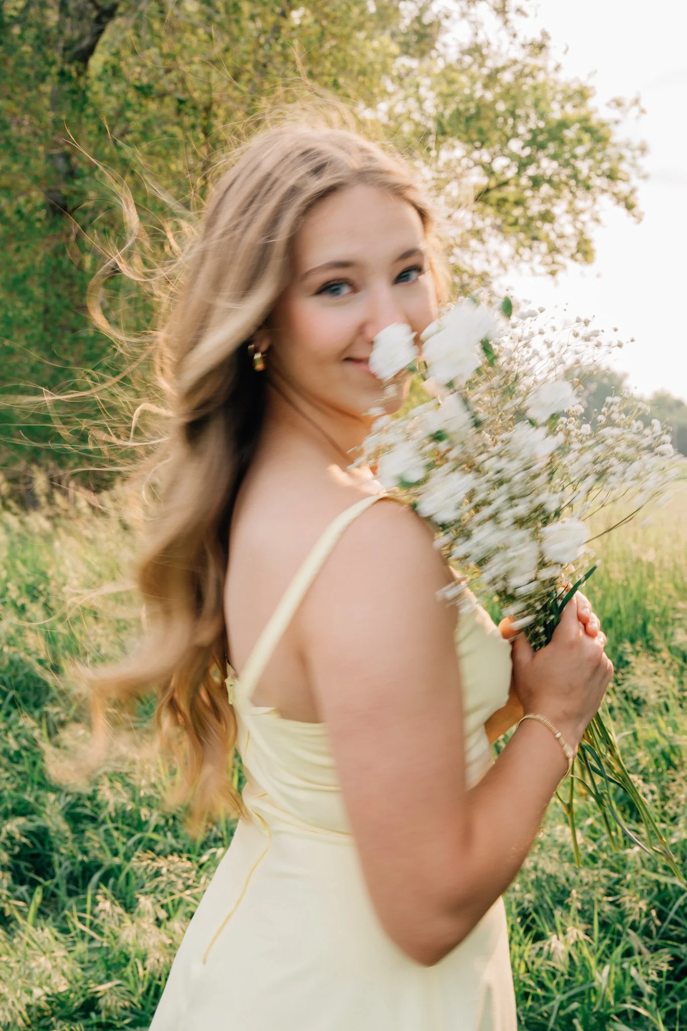 A motion blur image of a girl smelling flowers as he hair blows in the wind during her senior picture session.