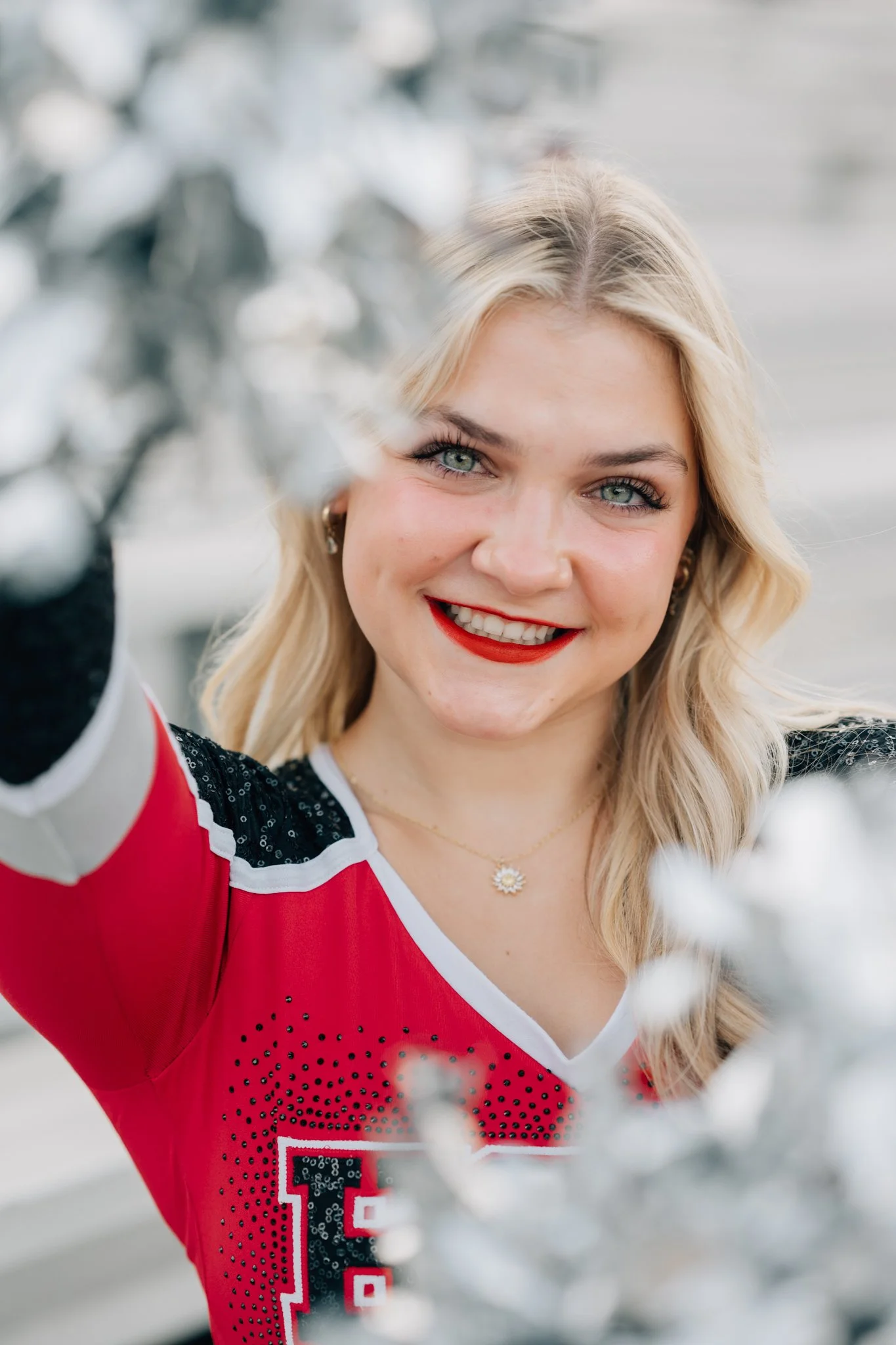 Close up of cheerleader holding her poms to camera, smiling for her senior pictures.