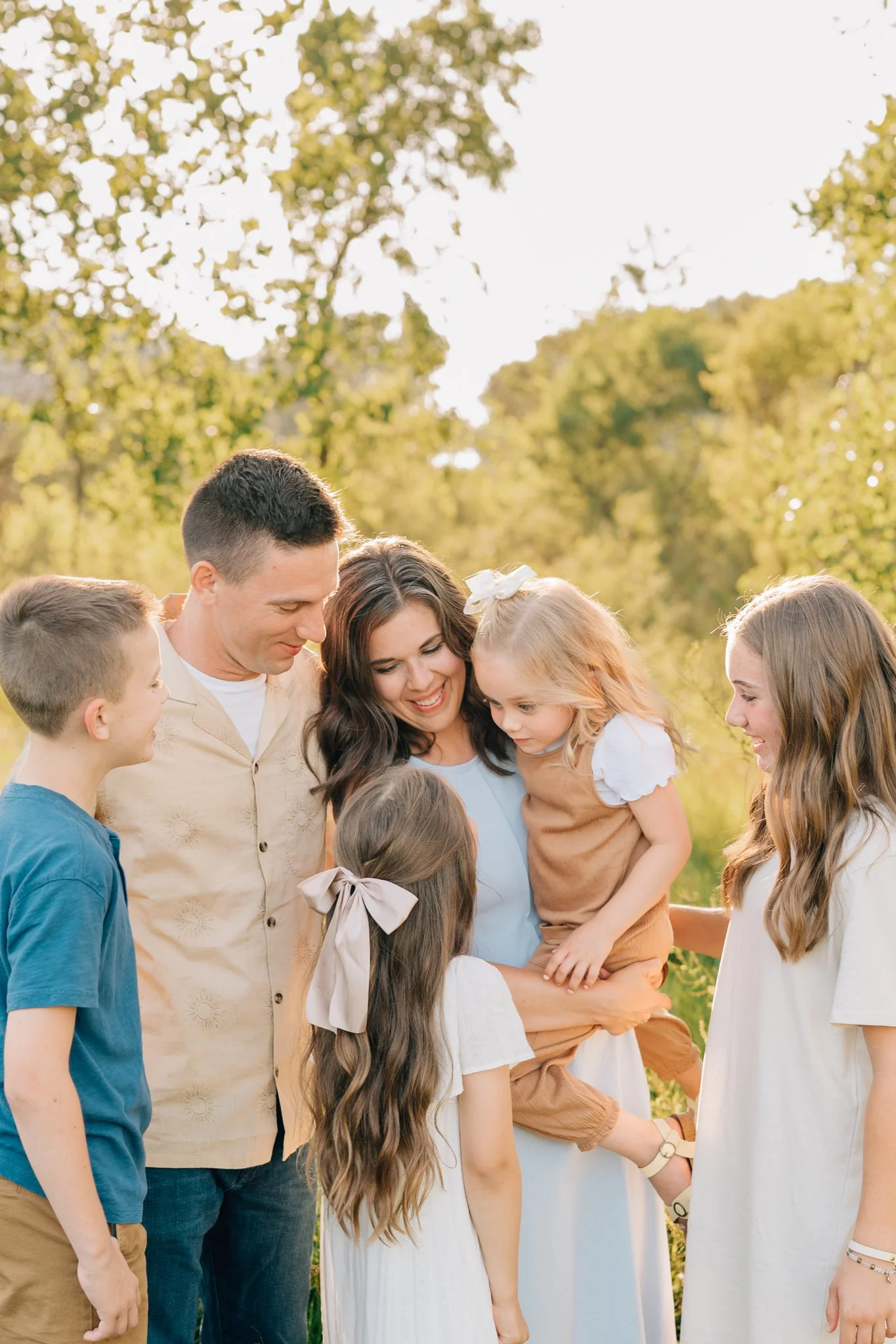 family admires youngest sister while mom holds her during family photos during golden hour.