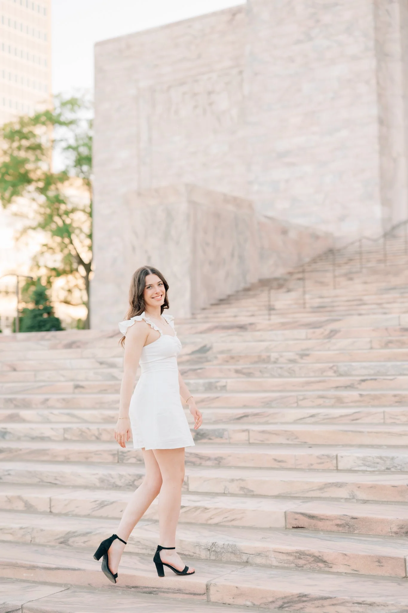 Girl in white dress walks up stairs of Jocelyn museum for her senior pictures in Omaha.