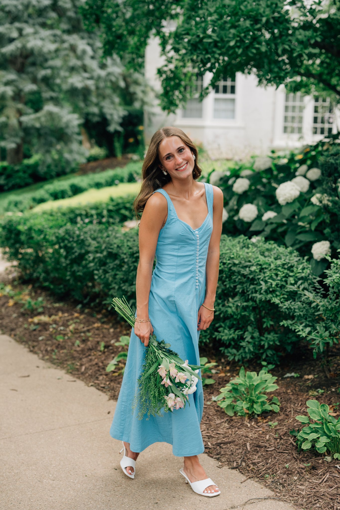 Girl wearing blue dress poses with flowers in Omaha for her summer senior picture session.