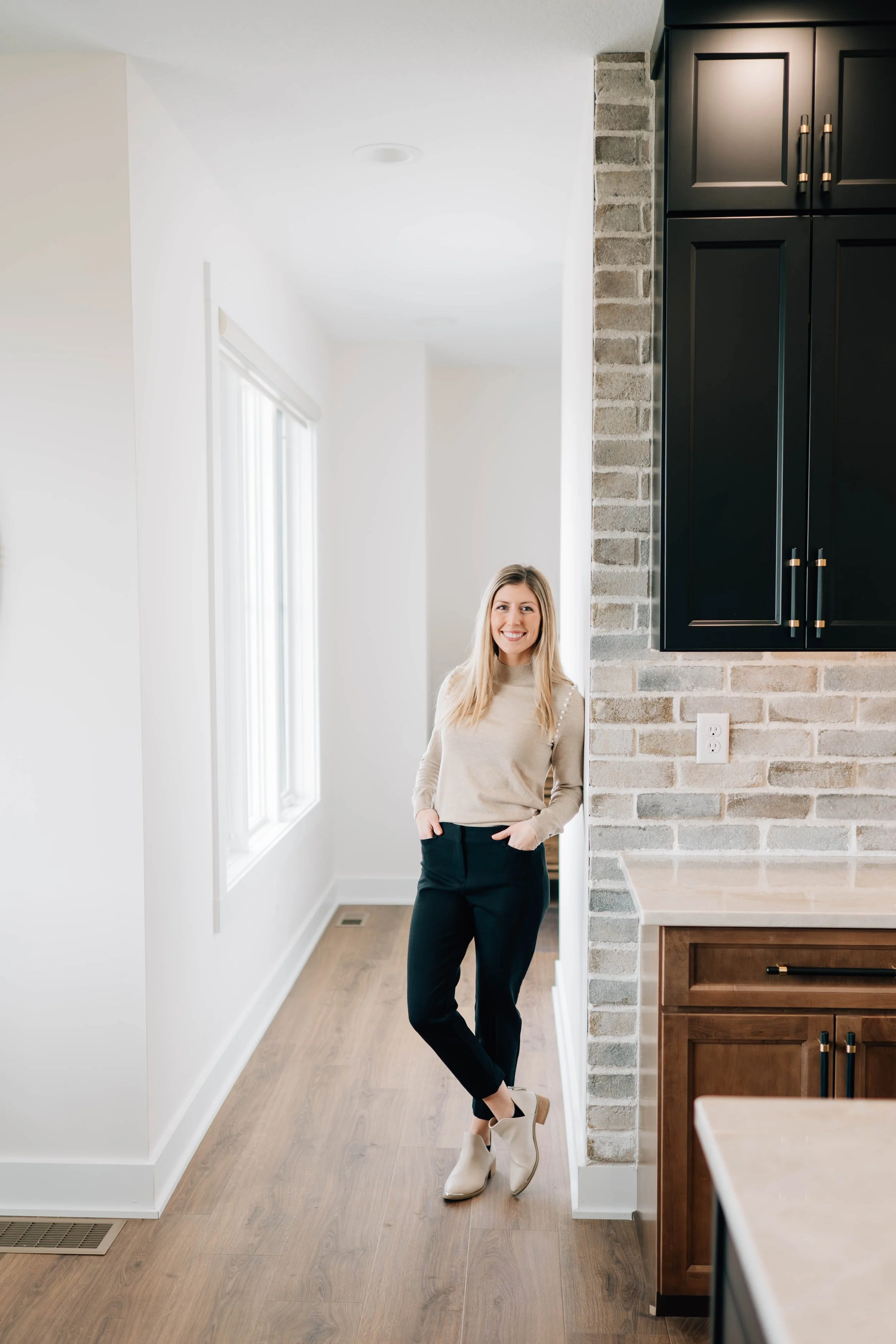 Woman leans against kitchen wall, smiles to camera for her realty headshot photo session.