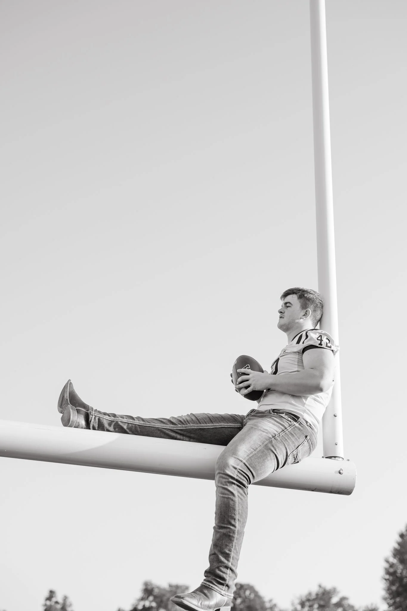 Senior guy sits on top of football goalpost for his senior pictures.