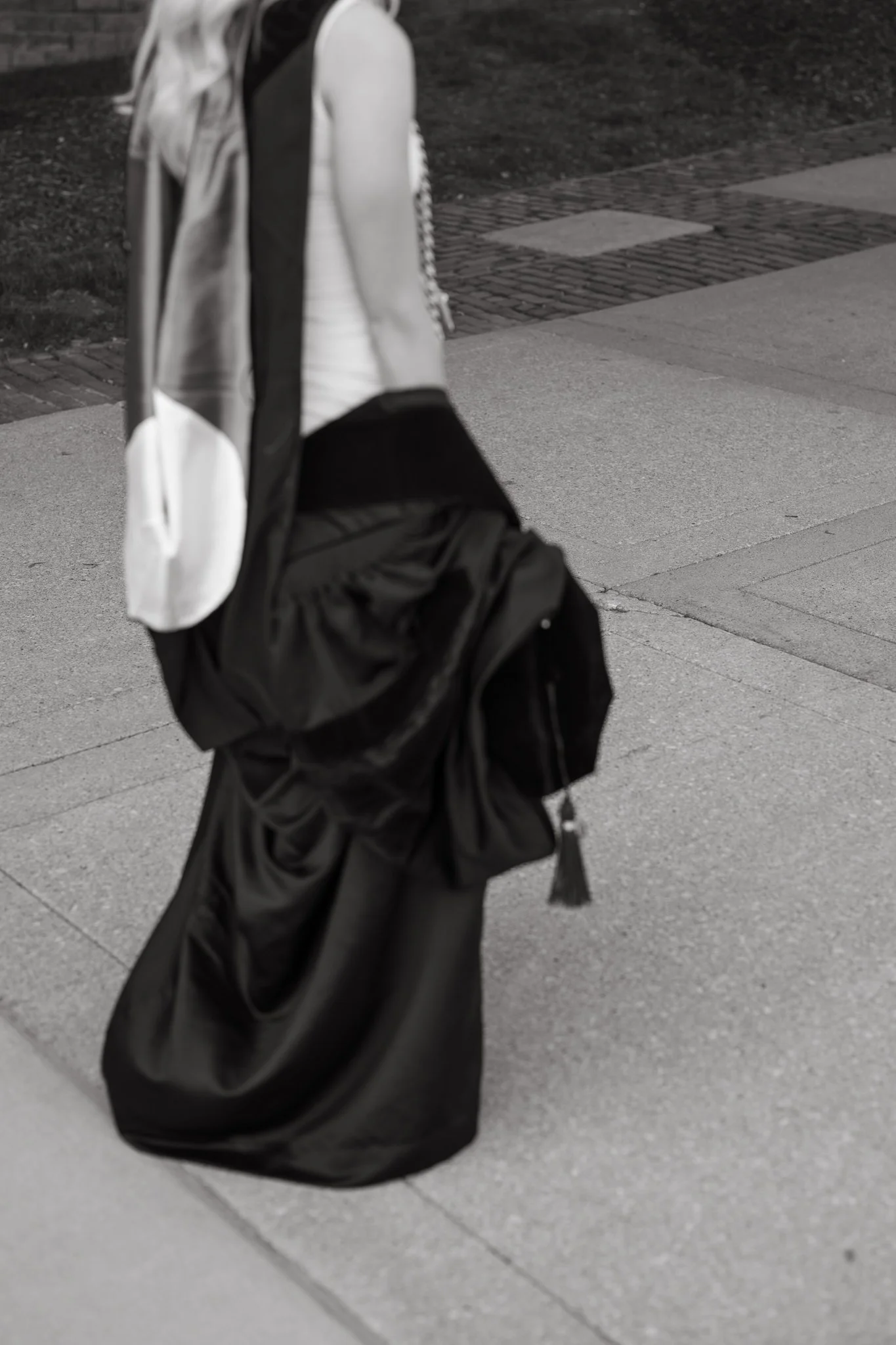 Detail photo of cap and gown in black and white as student walks along Creighton University campus in Omaha, NE.