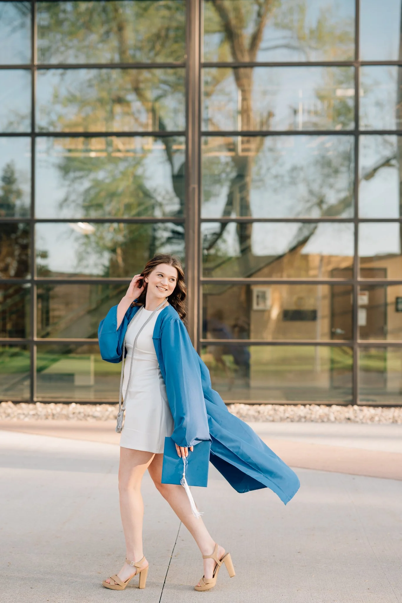 College graduate walks across campus in cap and gown for college graduation photography session.