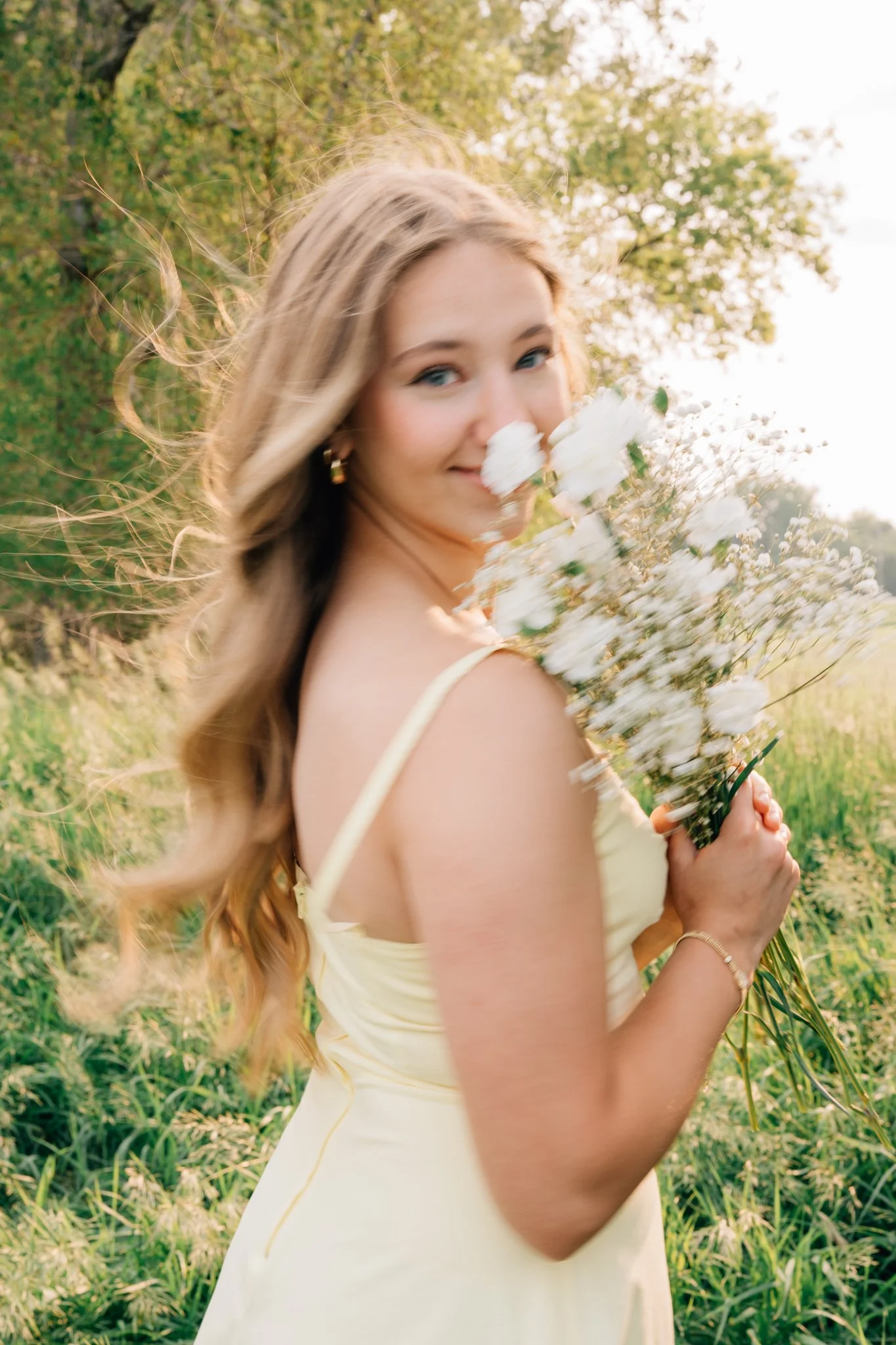 Motion blur image of a girl smelling flowers, hair blowing in the wind, posing for her senior pictures.
