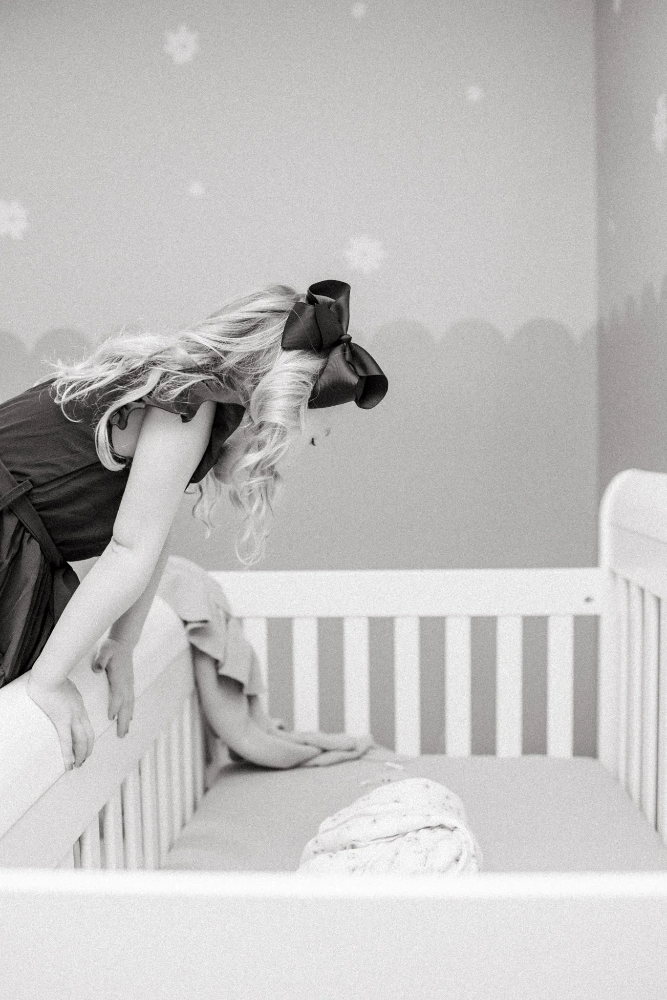 Big sister peeks into crib during lifestyle newborn photography session in Iowa.
