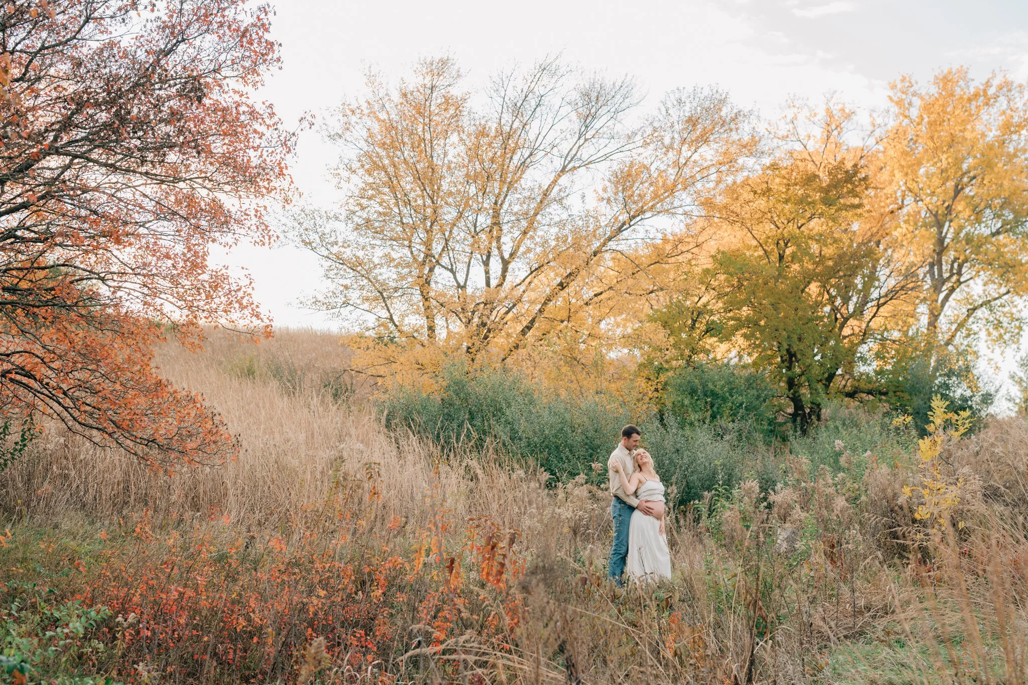 Couple poses in Iowa state park in the fall during their maternity photography session in Iowa.