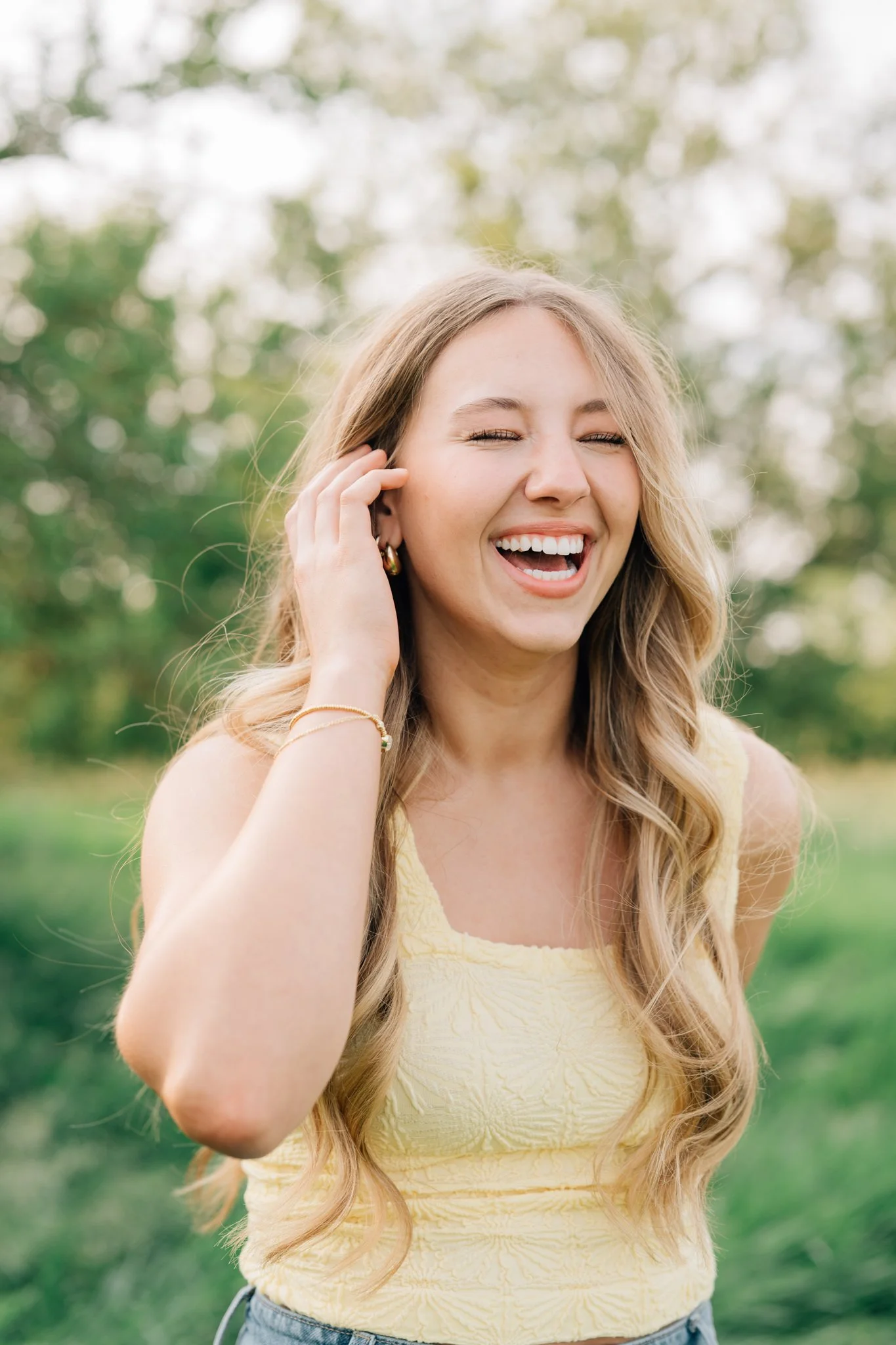 Candid photo of a girl laughing in a field, wearing butter yellow top for her senior photos.