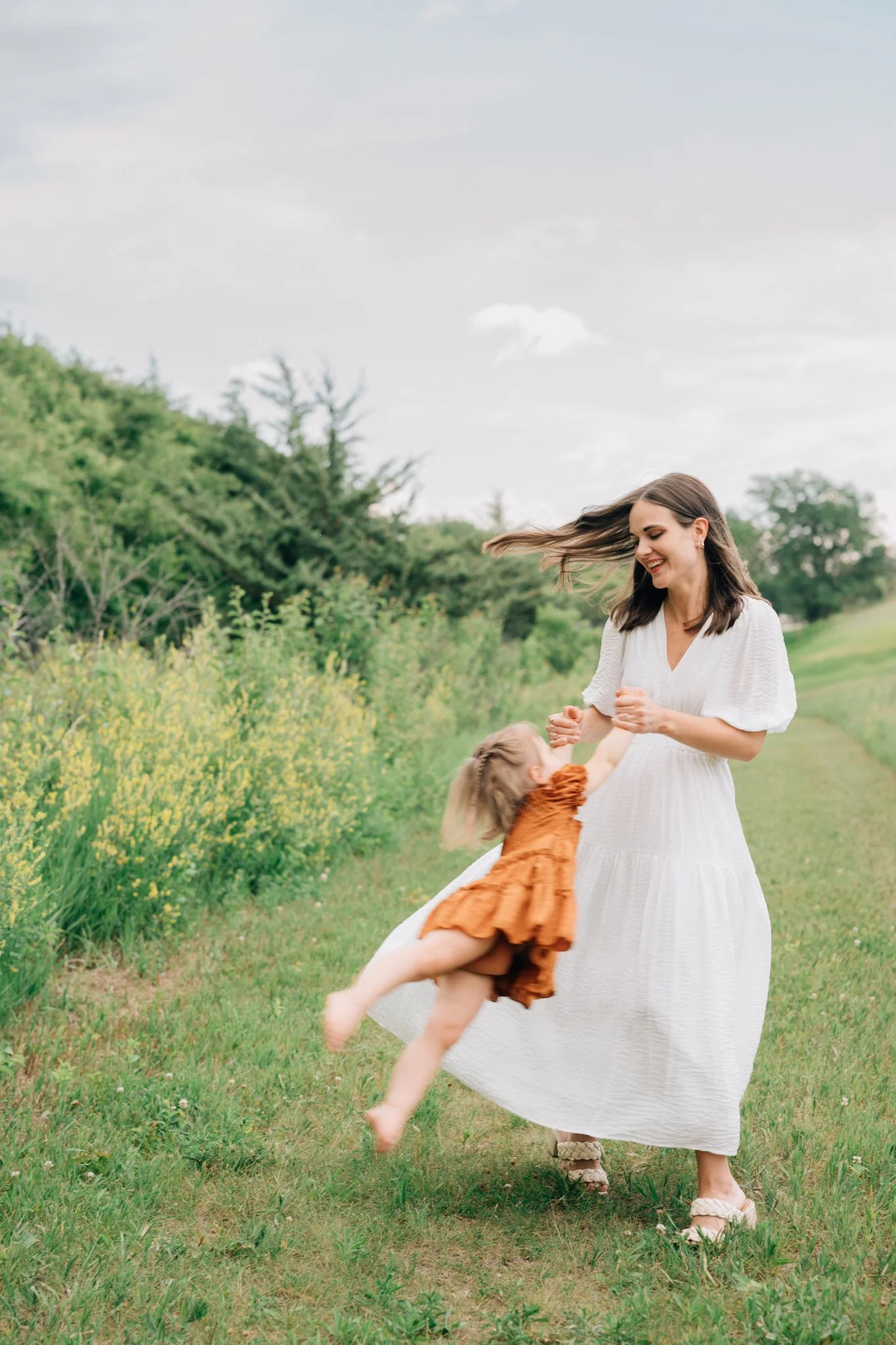 Mother twirls her young daughter during family picture session in Iowa on a cloudy night.