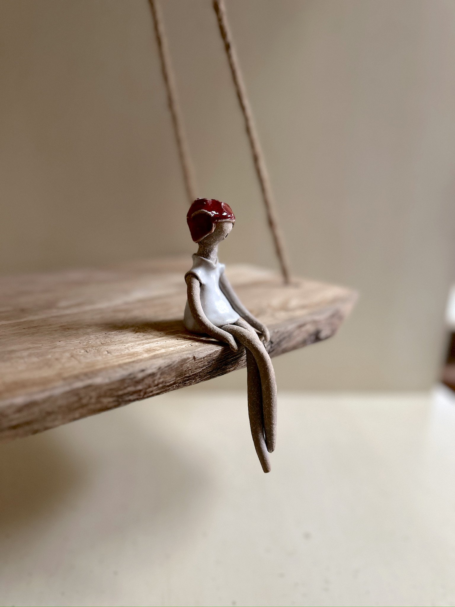 Glazed and Fired ceramic handmade sculpture of a lady with a red head wrap and sitting on the edge of a swing. Image from the right.