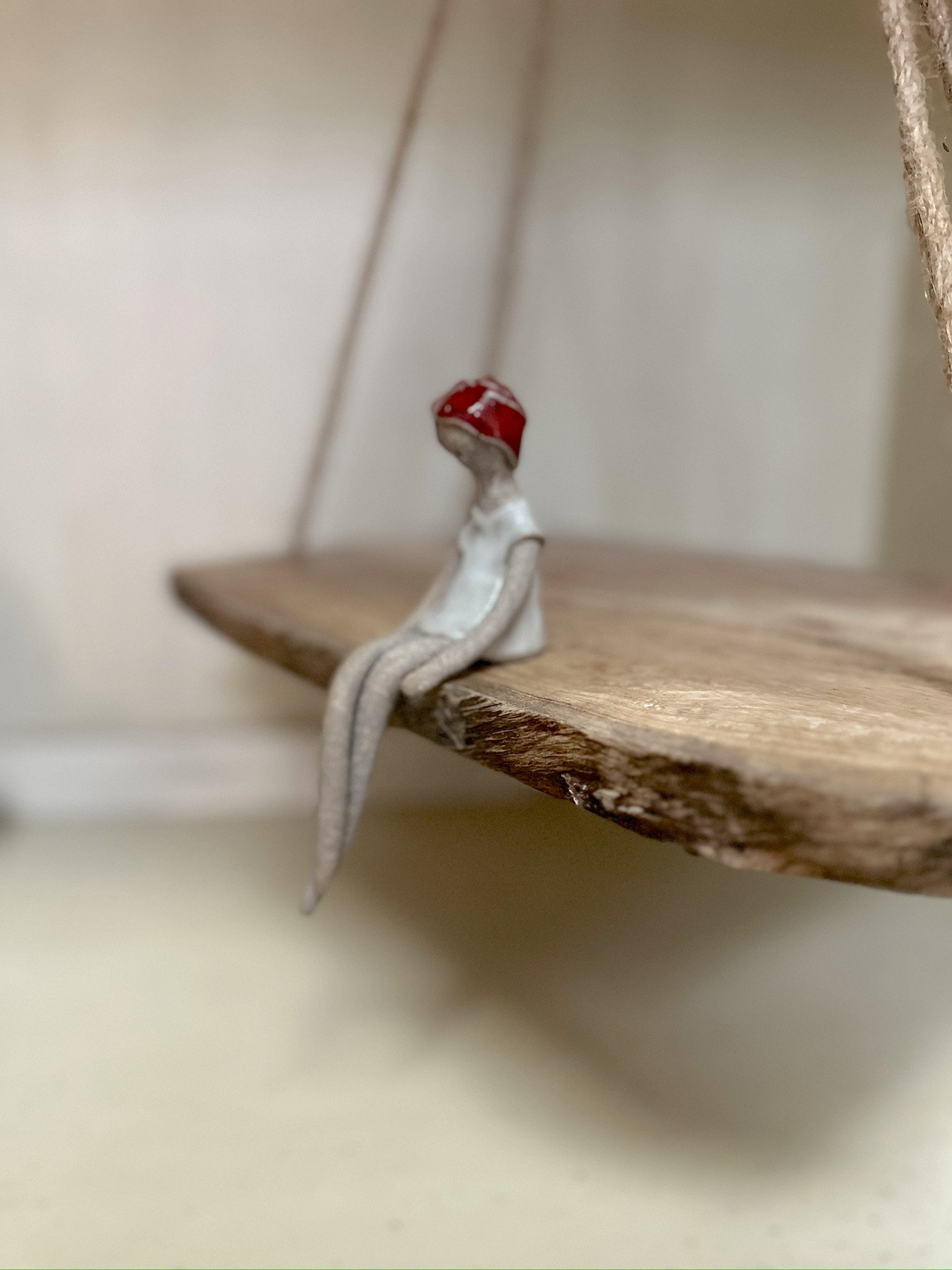 Glazed and Fired ceramic handmade sculpture of a lady with a red head wrap and sitting on the edge of a swing. Image from the left.