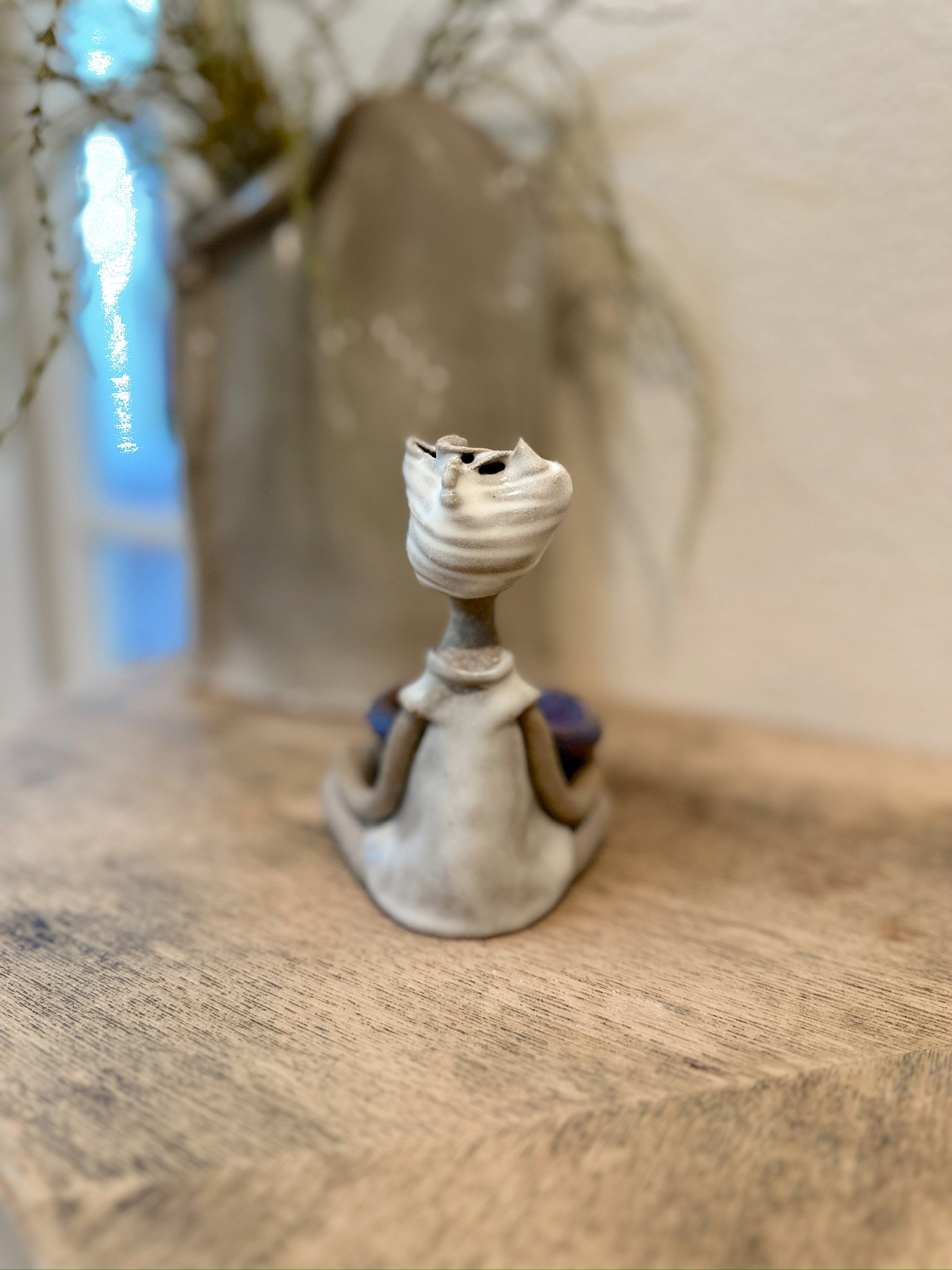 Glazed and Fired ceramic handmade sculpture of a lady holding a blue/purple bowl and sitting on a table. Image from the back.