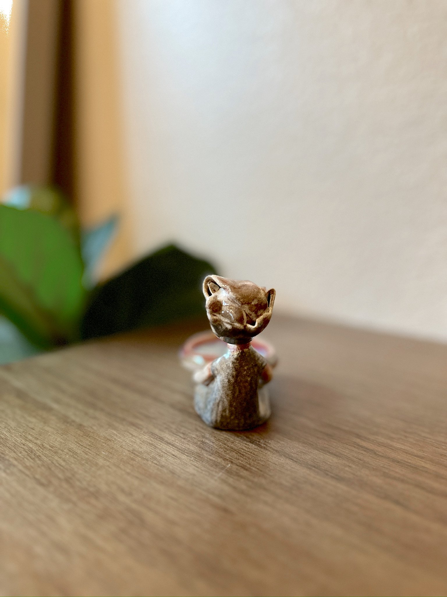 Glazed and Fired ceramic handmade sculpture of a lady holding a red and blue plate and sitting on a table. Image from the back.