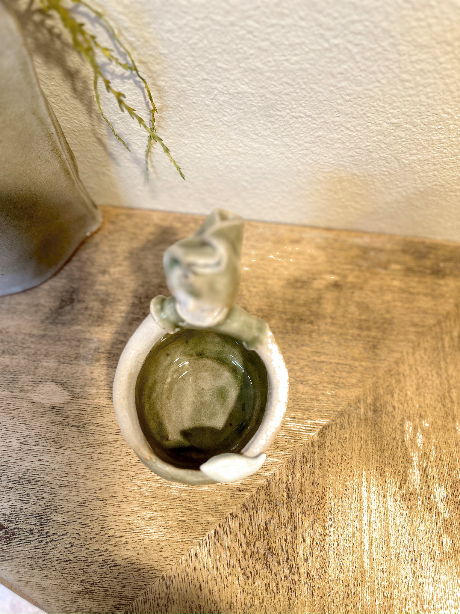 Glazed and Fired ceramic handmade sculpture of a sage green lady whose bottom half is a bowl with a white bird sitting on the edge and sitting on a table. Image from the top.