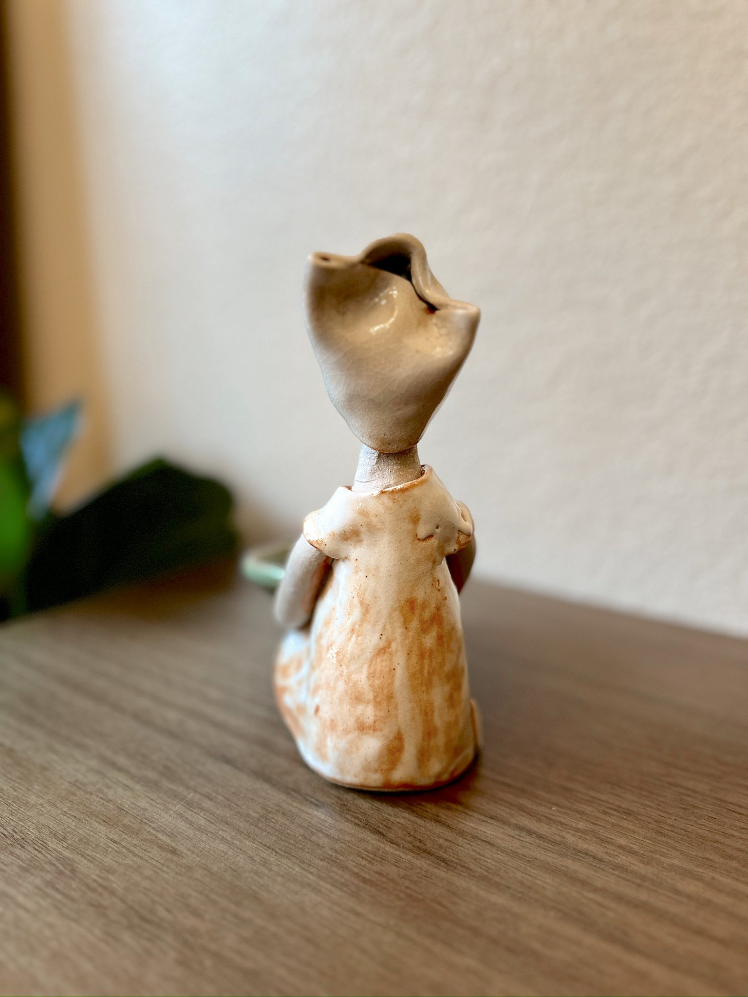 Glazed and Fired ceramic handmade sculpture of a lady holding a sage green bowl and sitting on a table. Image from the back.