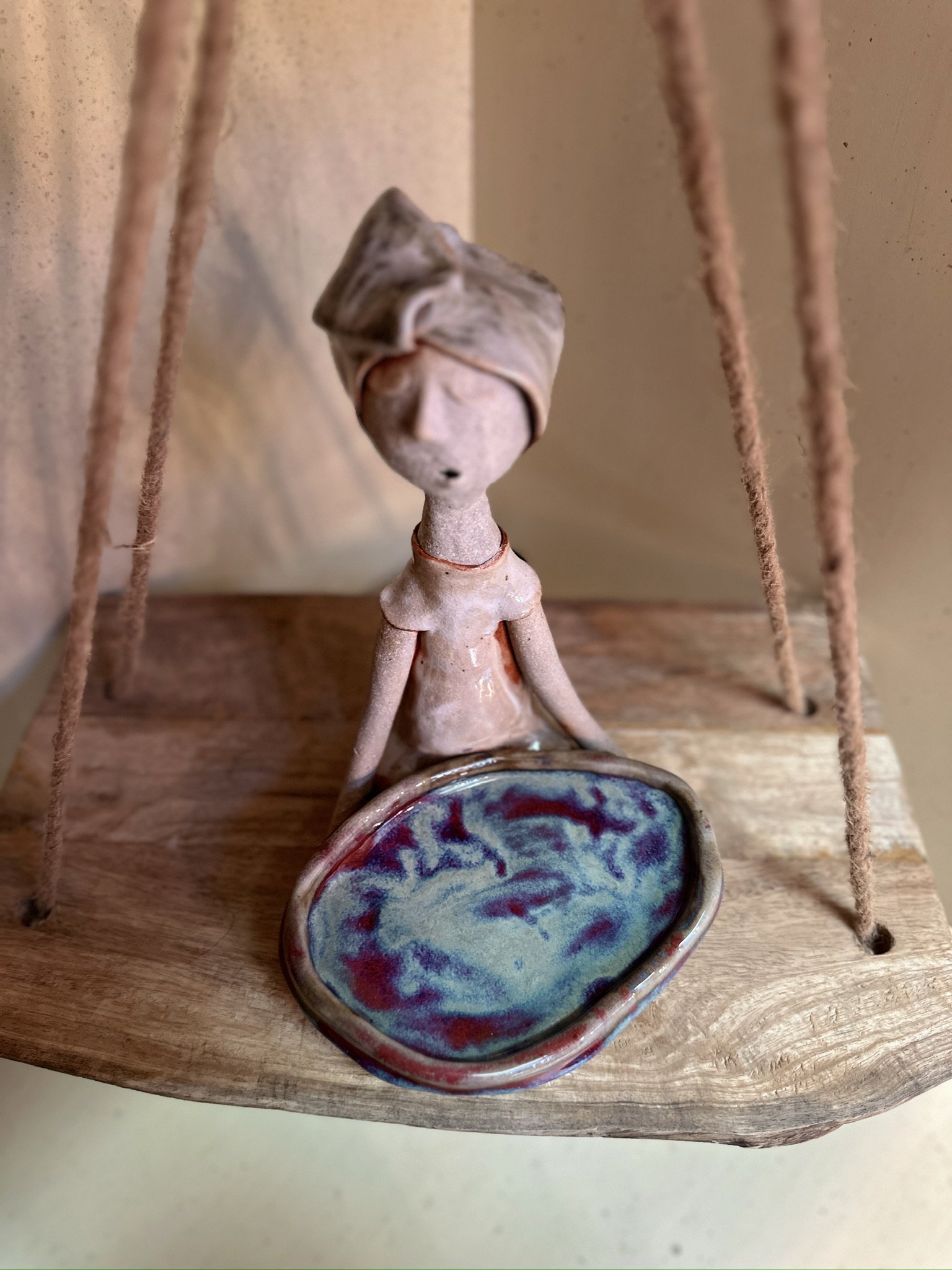 Glazed and Fired ceramic handmade sculpture of a lady holding a large purple and blue plate and sitting on a table. Image from the top.