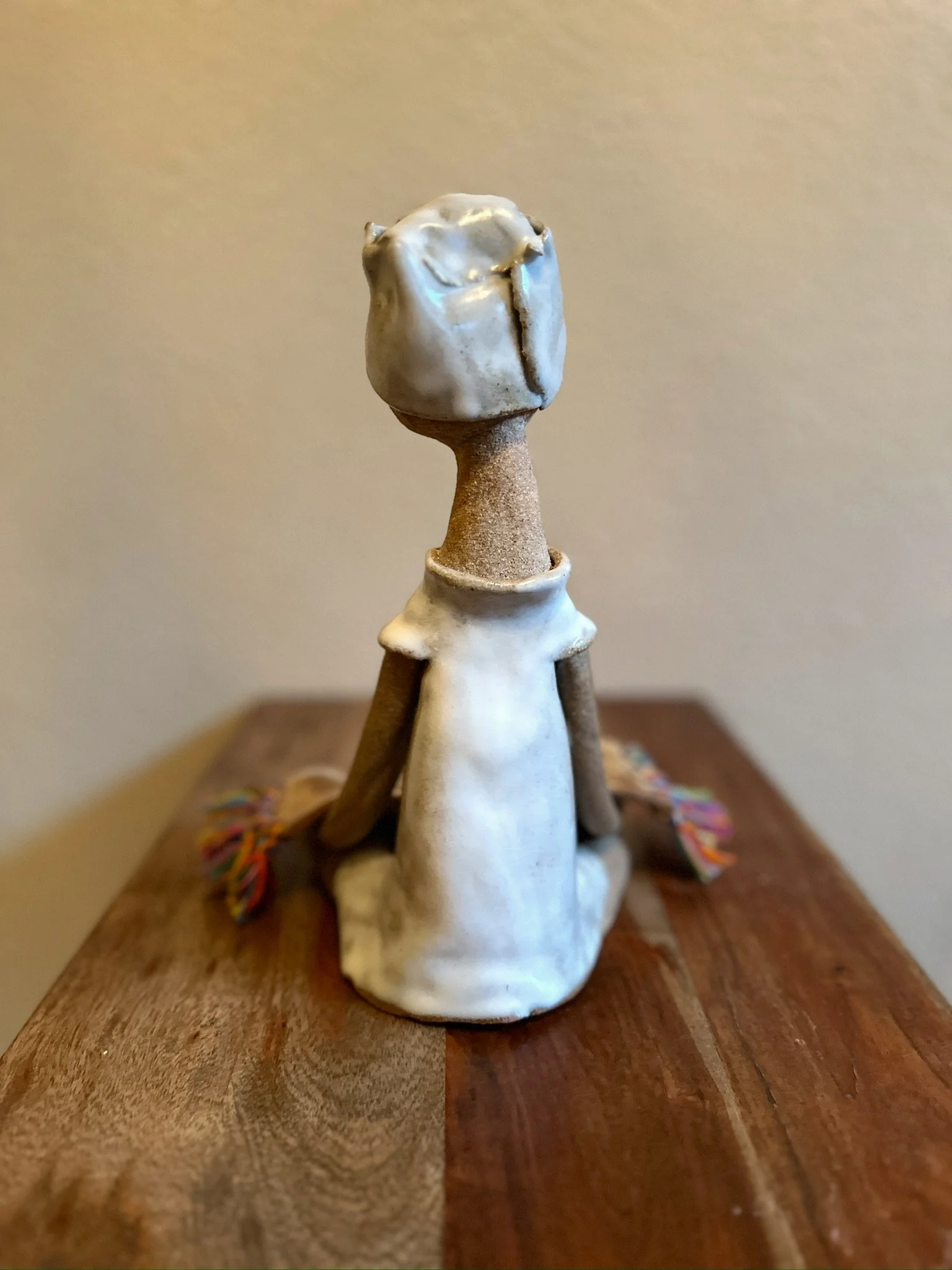 Glazed and Fired ceramic handmade sculpture of a lady holding a large plate with rainbow tassels and sitting on a table. Image from the back.
