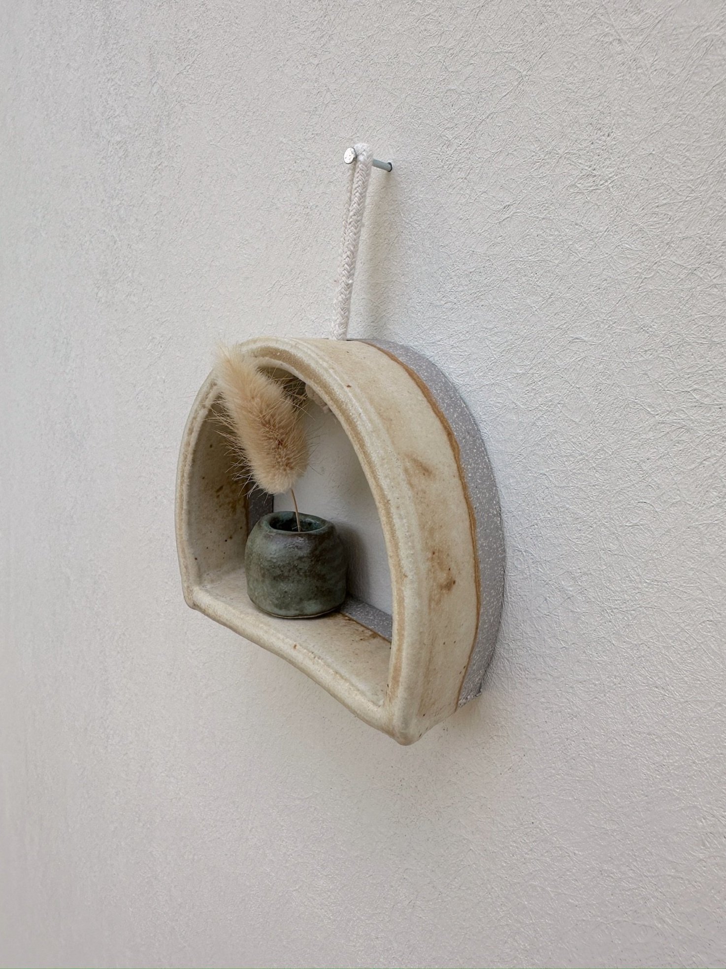 Glazed and Fired ceramic handmade rounded frame with a flat bottom with a small blue/green vase. Image from the right.