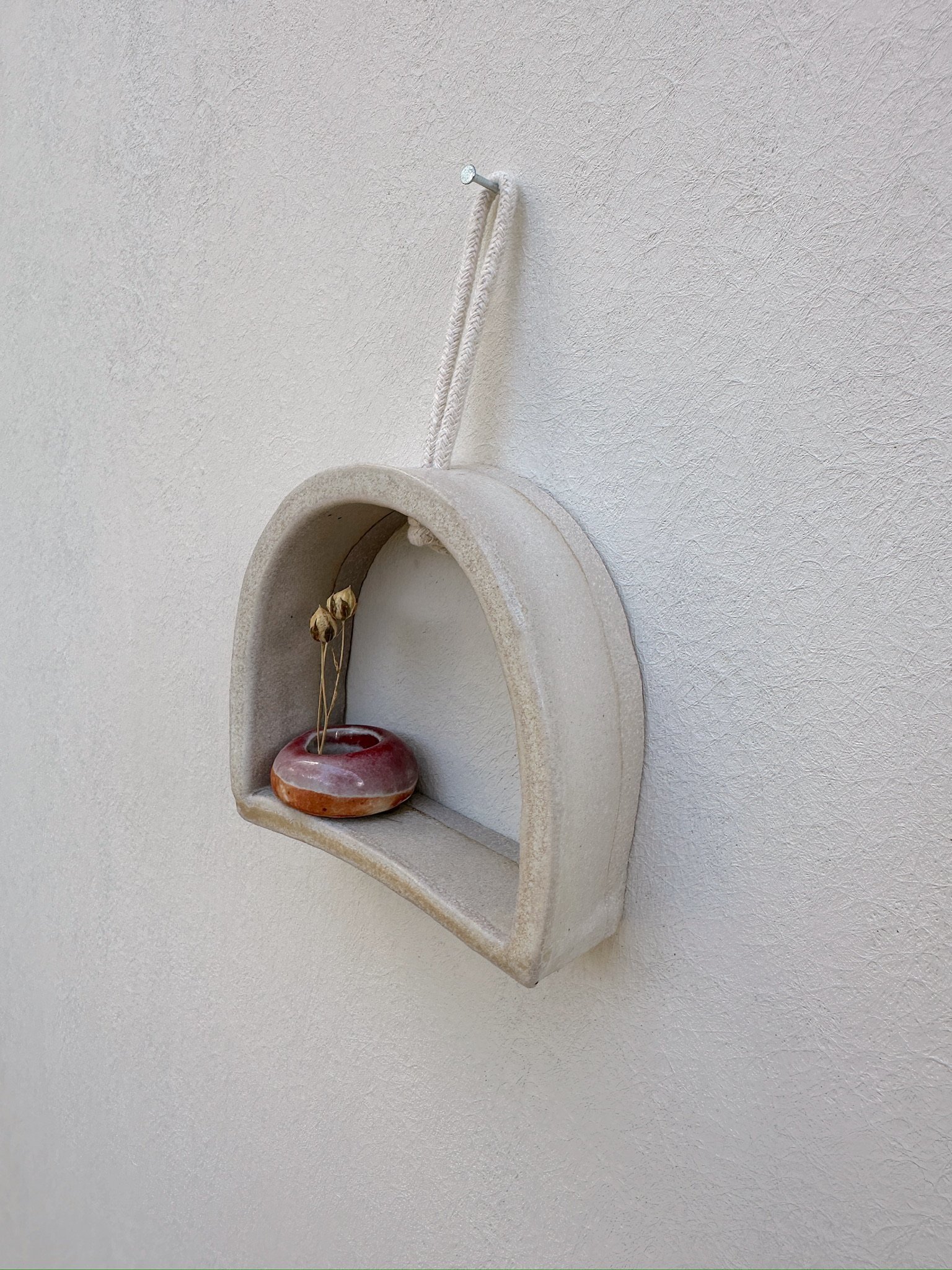 Glazed and Fired ceramic handmade rounded frame with a flat bottom with a small red vase. Image from the right.