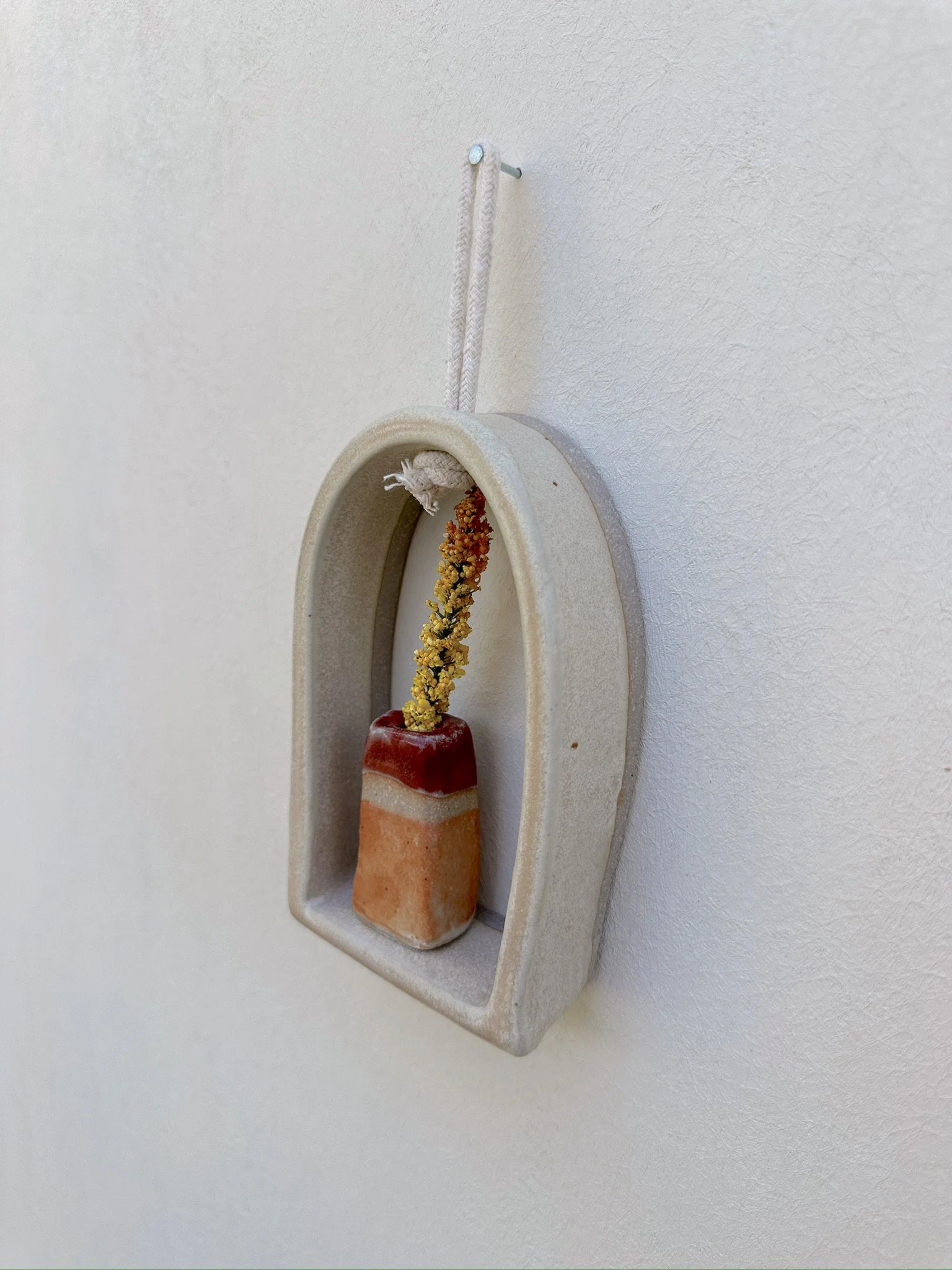 Glazed and Fired ceramic handmade rounded frame with a flat bottom with a small orange and red vase. Image from the right.