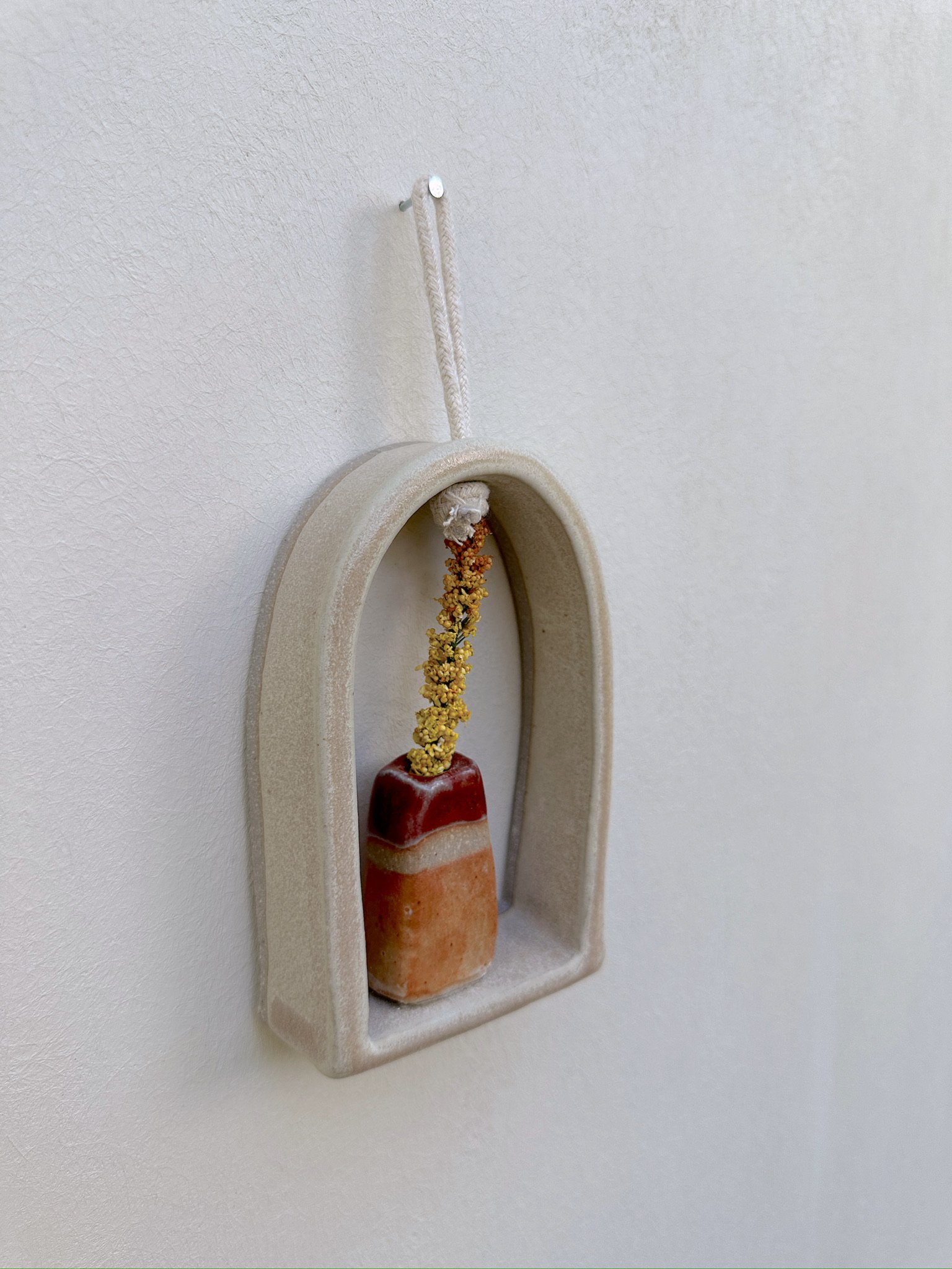 Glazed and Fired ceramic handmade rounded frame with a flat bottom with a small orange and red vase. Image from the left.