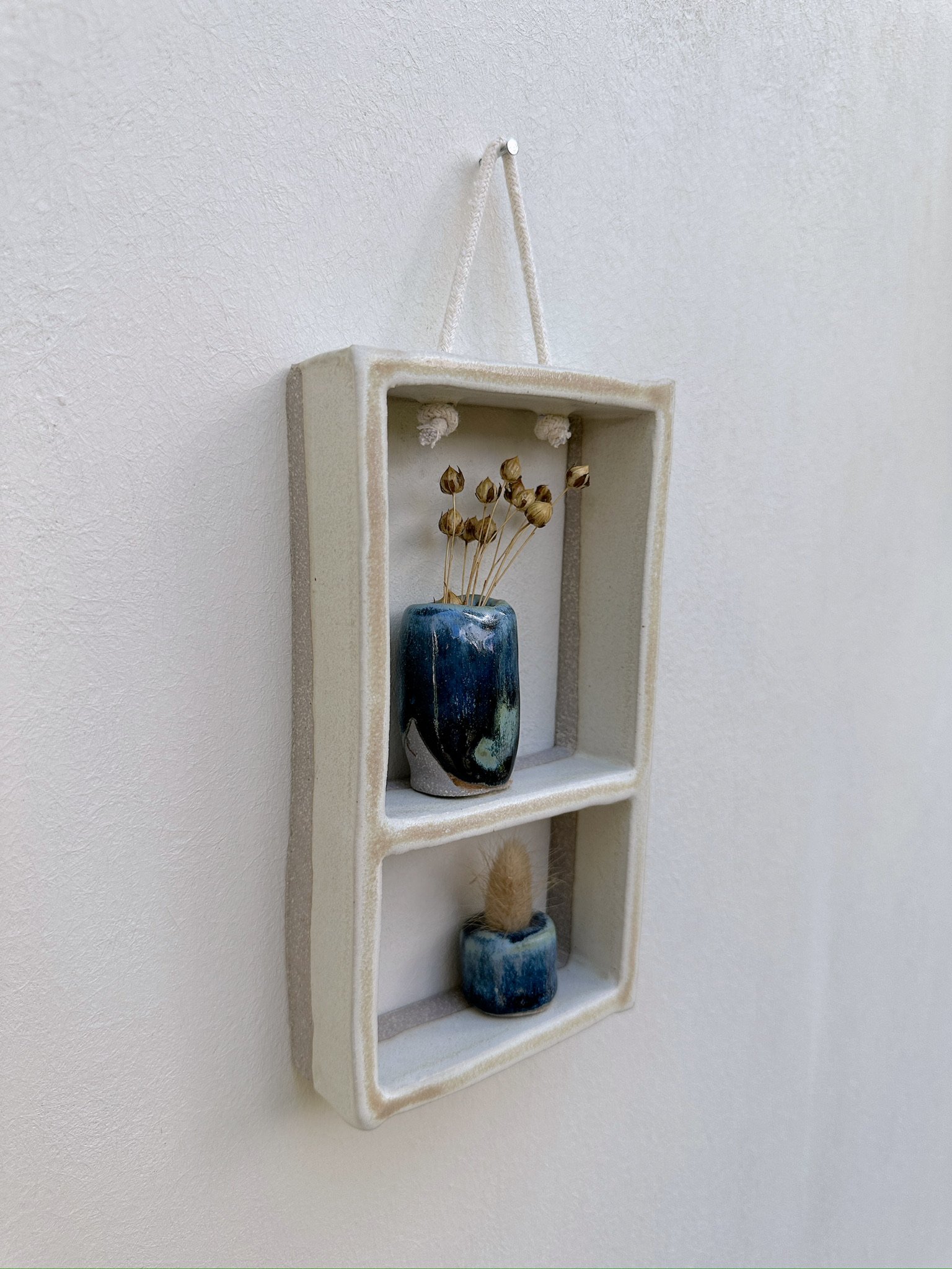 Glazed and Fired ceramic handmade two-tiered frame with two small blue vases. Image from the left.
