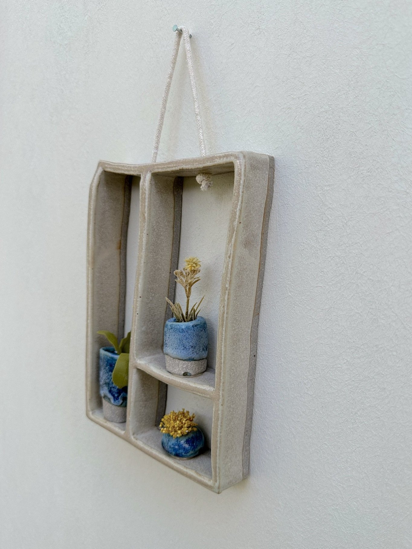 Glazed and Fired ceramic handmade three-tiered frame with three small blue vases. Image from the right.