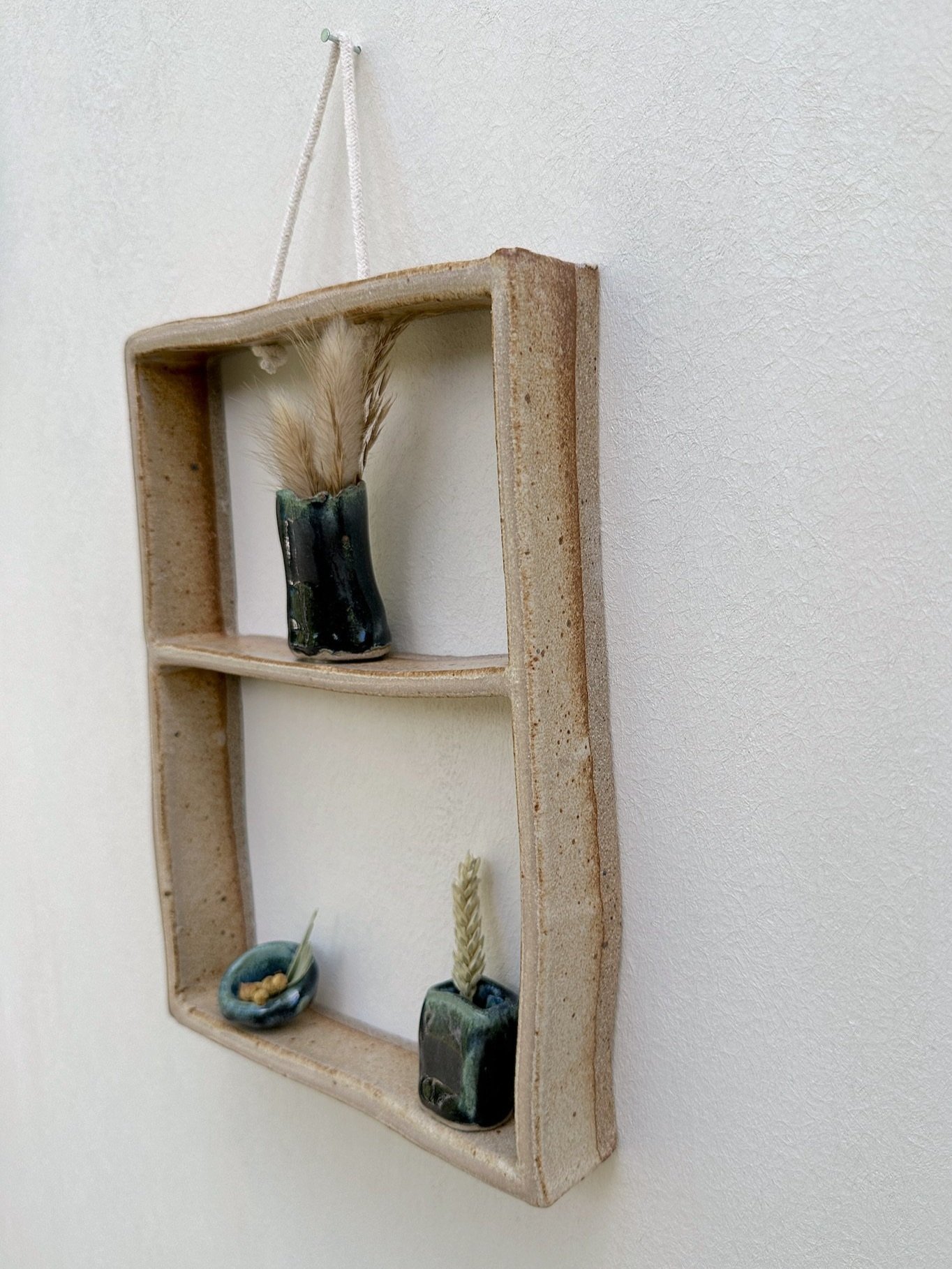 Glazed and Fired ceramic handmade two-tiered frame with three dark blue vases. Image from the right.