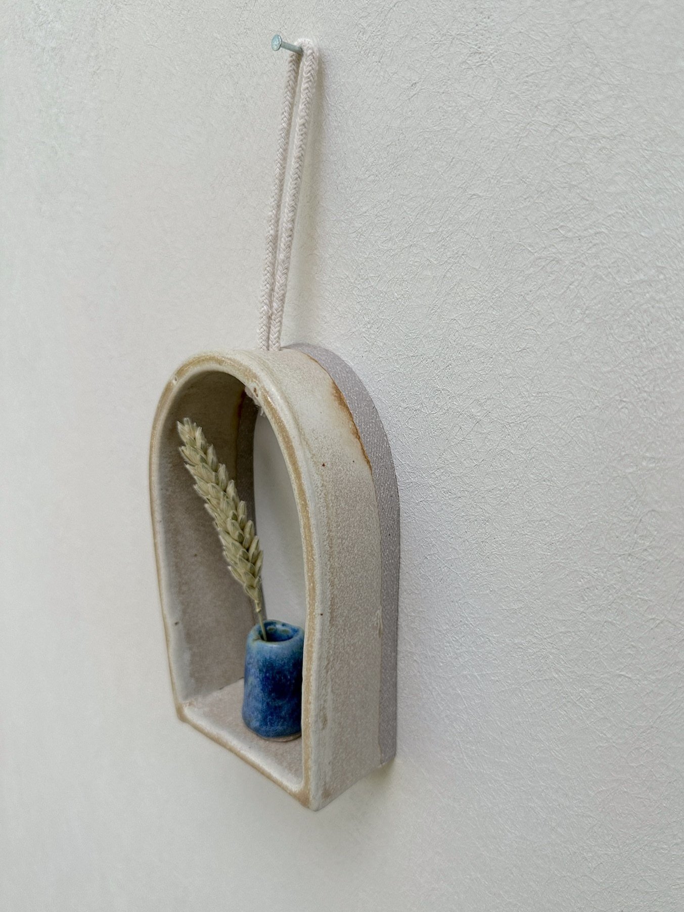 Glazed and Fired ceramic handmade rounded frame with a flat bottom with a small blue vase. Image from the right
