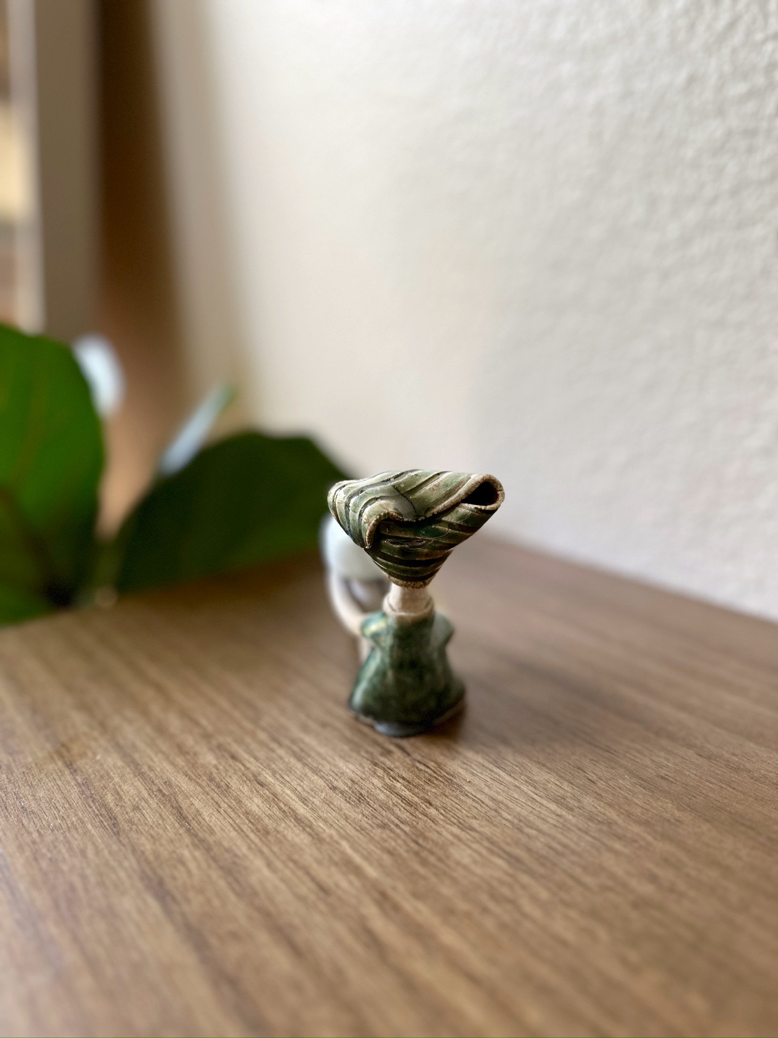 Glazed and Fired ceramic handmade sculpture of a lady with with her legs bend, holding a small incense holder and sitting on a table. Image from the back.