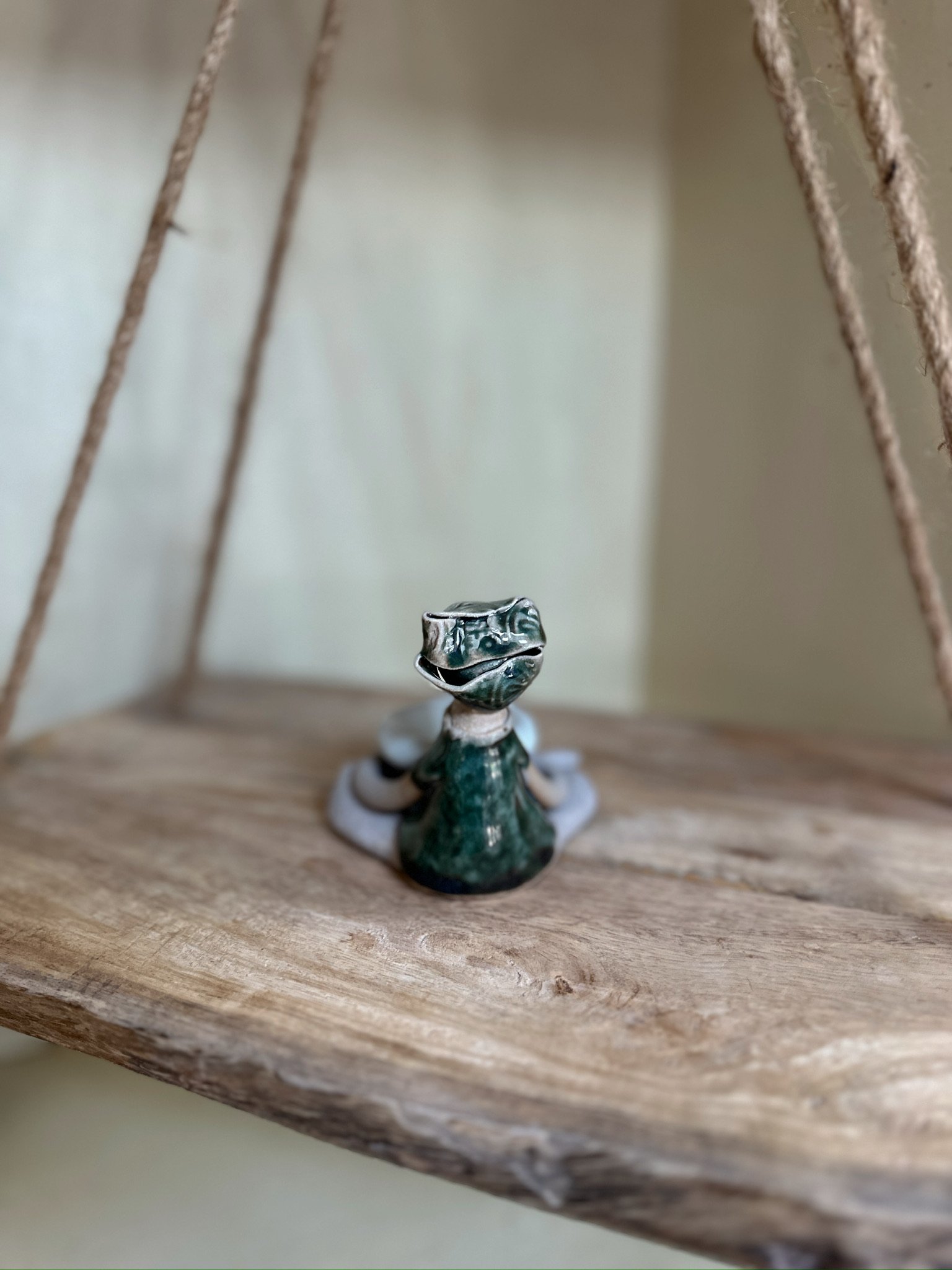 Glazed and Fired ceramic handmade sculpture of a lady holding a small bowl and sitting on a swing. Image from the top.
