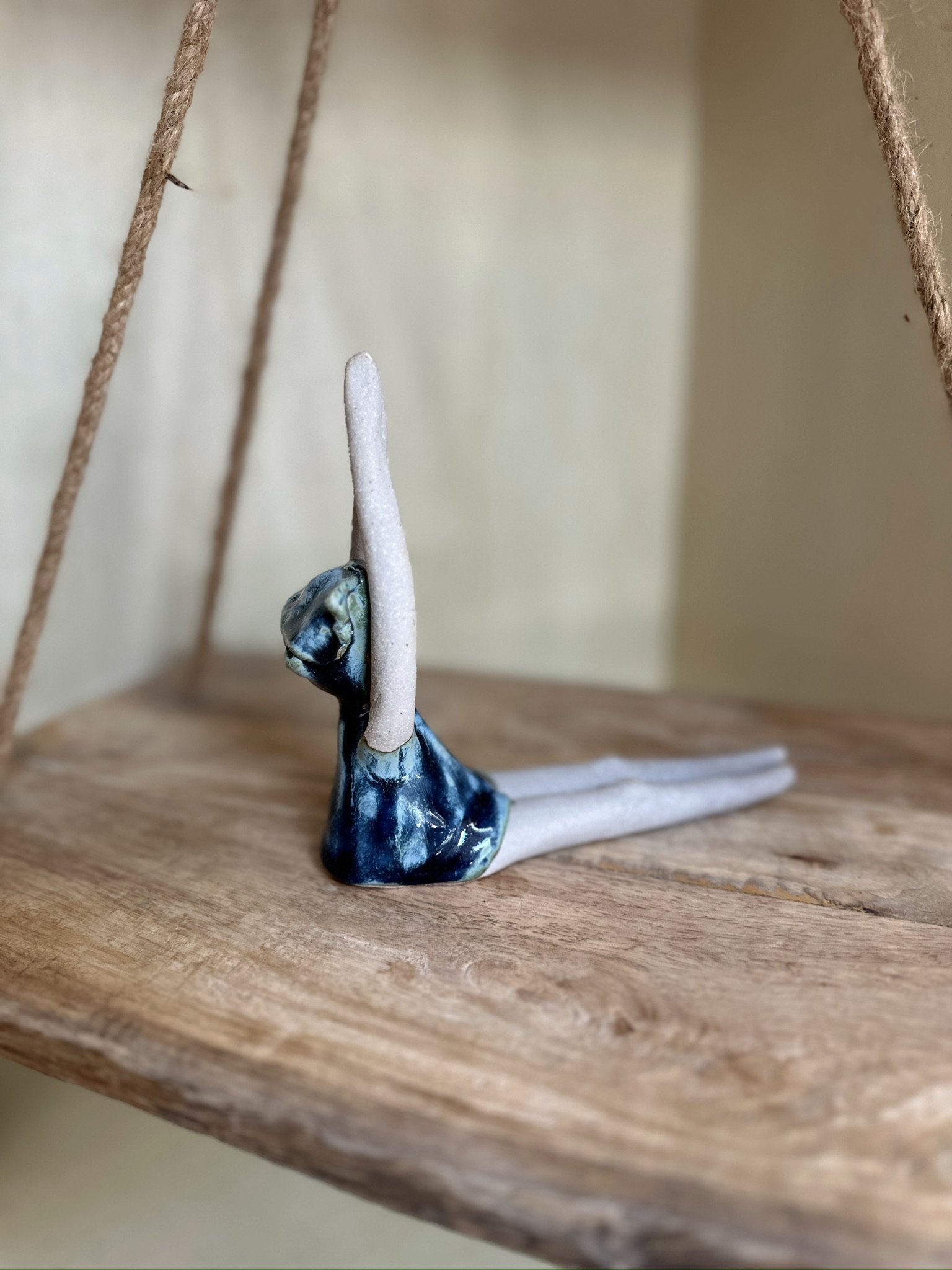 Glazed and Fired ceramic handmade sculpture of a lady sitting on a swing. Image from the right.