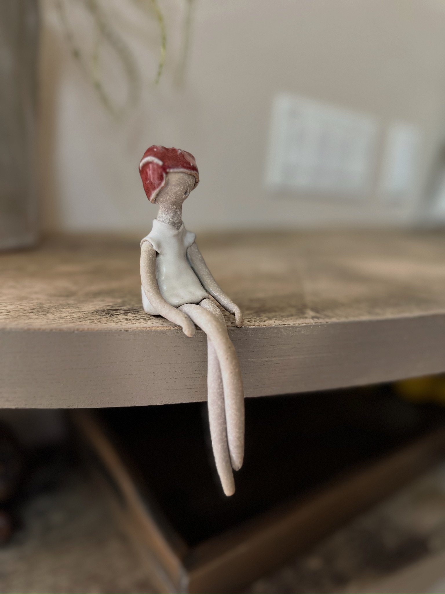 Glazed and Fired ceramic handmade sculpture of a lady with a red head wrap and sitting on the edge of a table. Image from the right.