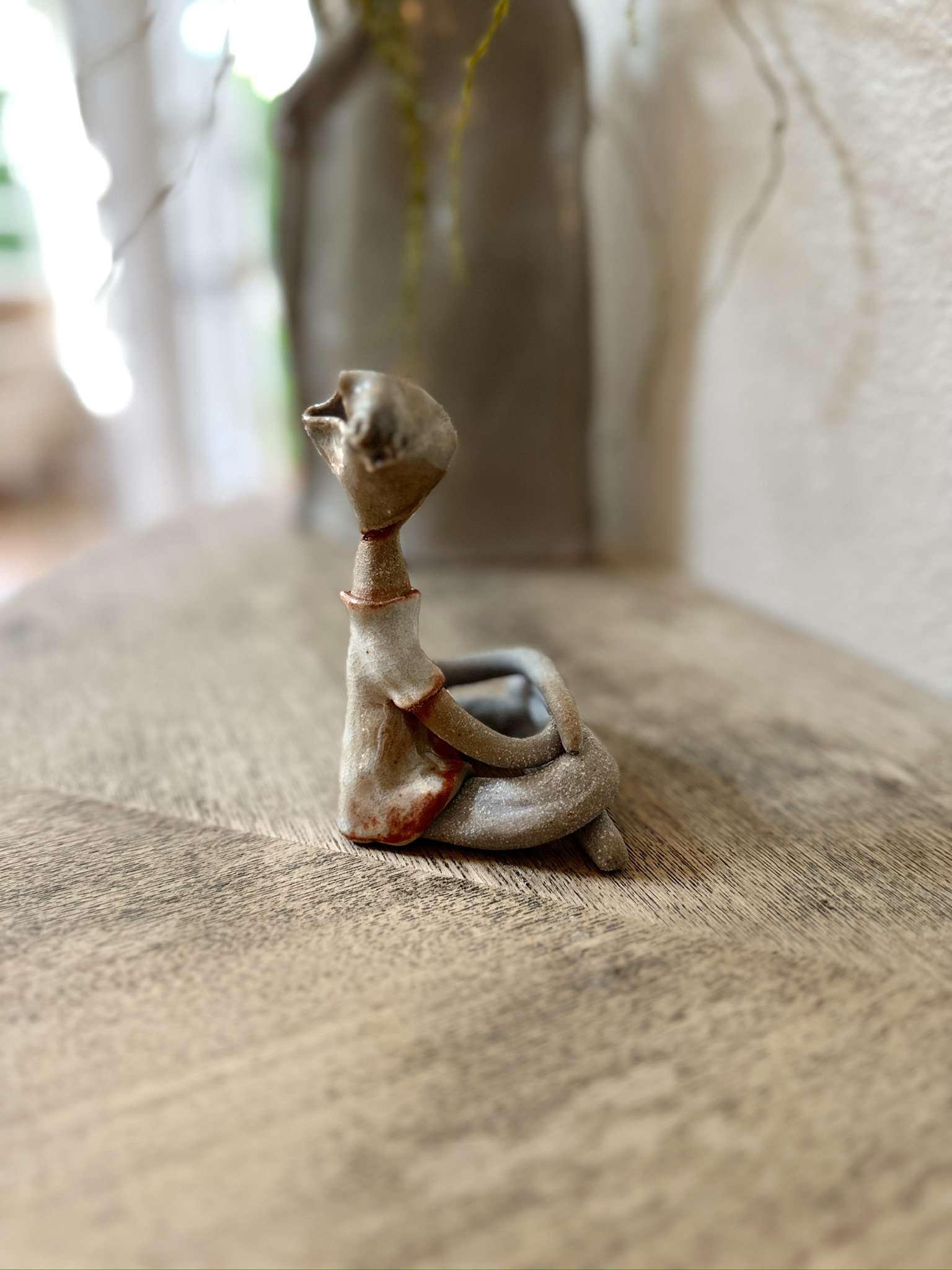 Glazed and Fired ceramic handmade sculpture of a lady with a beige head wrap and sitting cross-legged on a table. Image from the right.